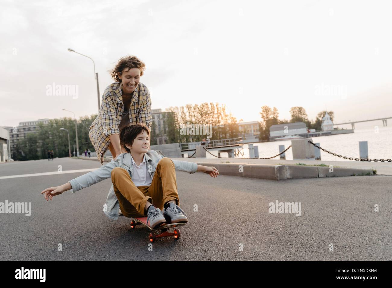 Happy mother riding her son on a skateboard. Mom and kid having fun in  their leisure time with skate Stock Photo - Alamy