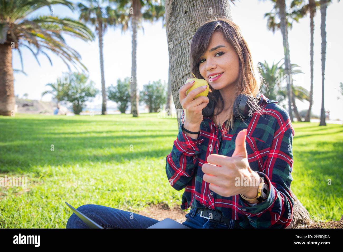 Young vegan woman eats an apple and gives thumbs up, photo with copy space. Stock Photo