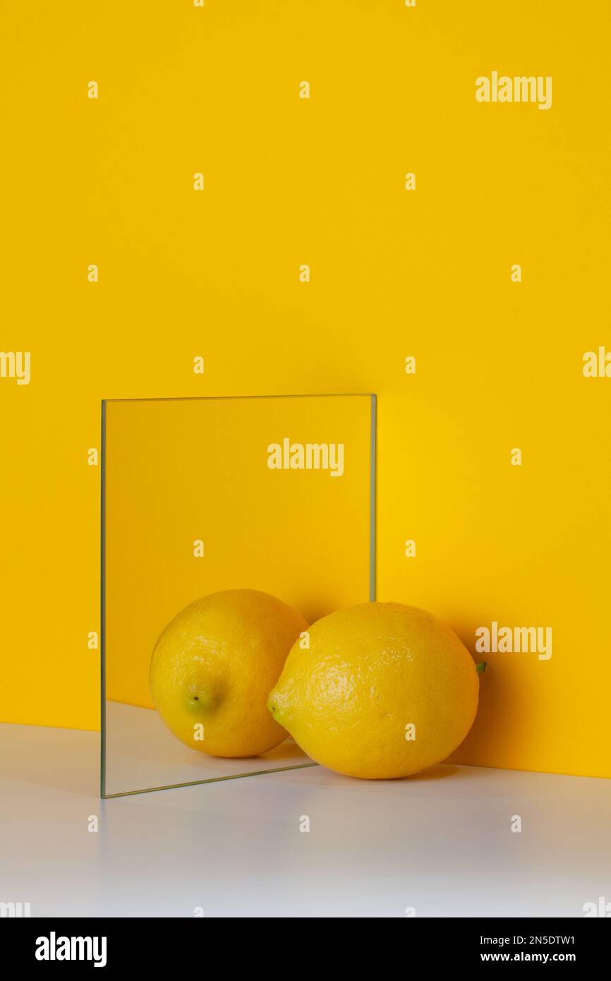 Yellow lemon is reflected in a mirror on a yellow background with copy
