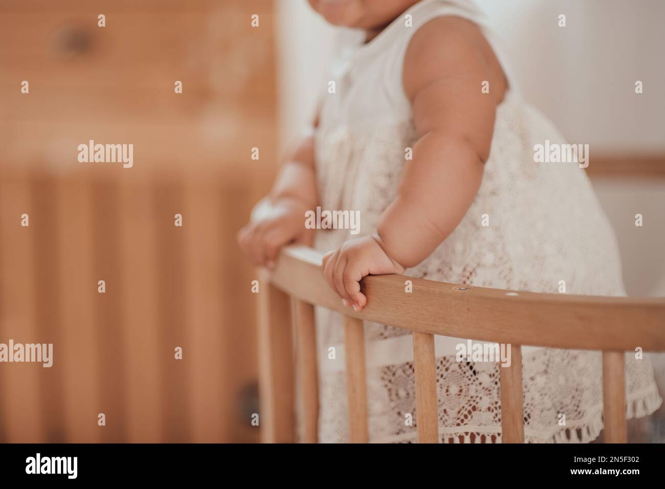 Candid authentic baby hands of cute african american diverse female child at home interior of earth colors. Swarthy infant girly stands in kids bed in Stock Photo