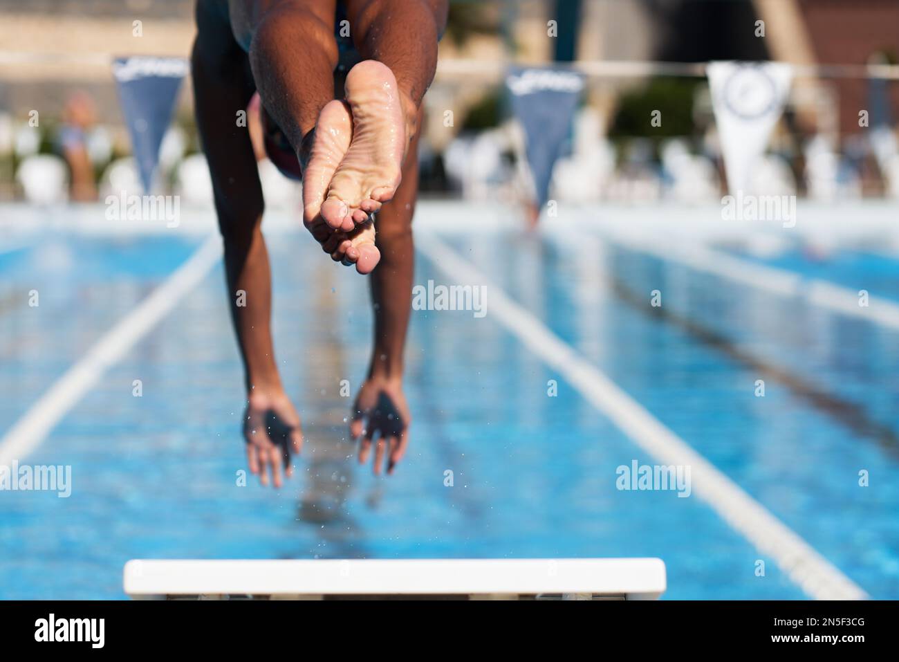 Male swimmer jumps off starting block and start swims in pool Stock