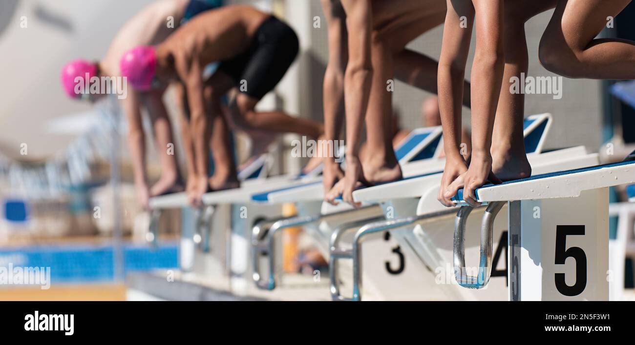 Teenage children on the starting blocks ready to dive into the pool at