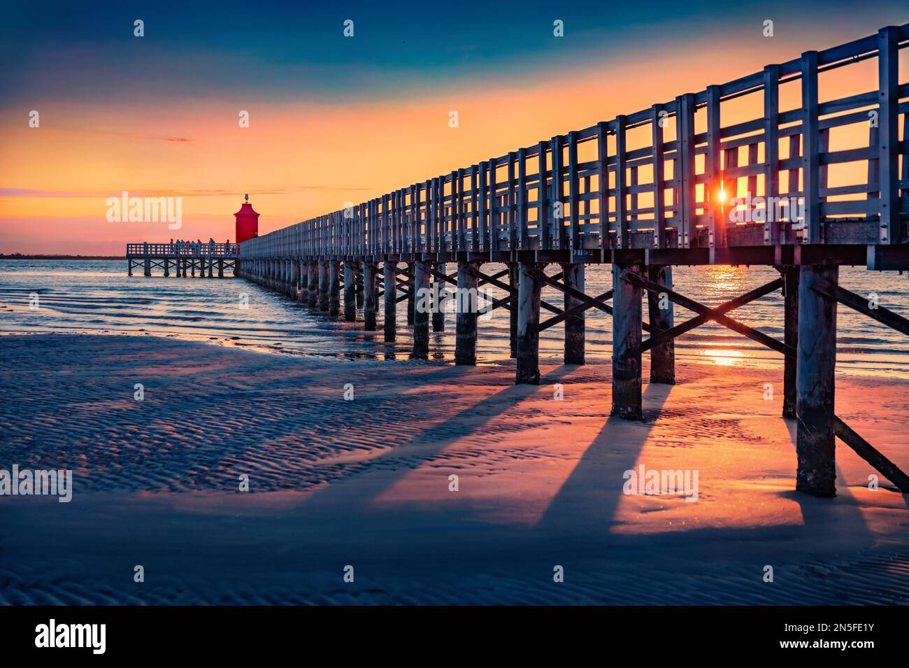 Fantastic sunrise in Lignano Sabbiadoro port. Colorful outdoor scene of Adriatic coast of Italy with lighthous and old wooden pier. Stunnig morning se Stock Photo