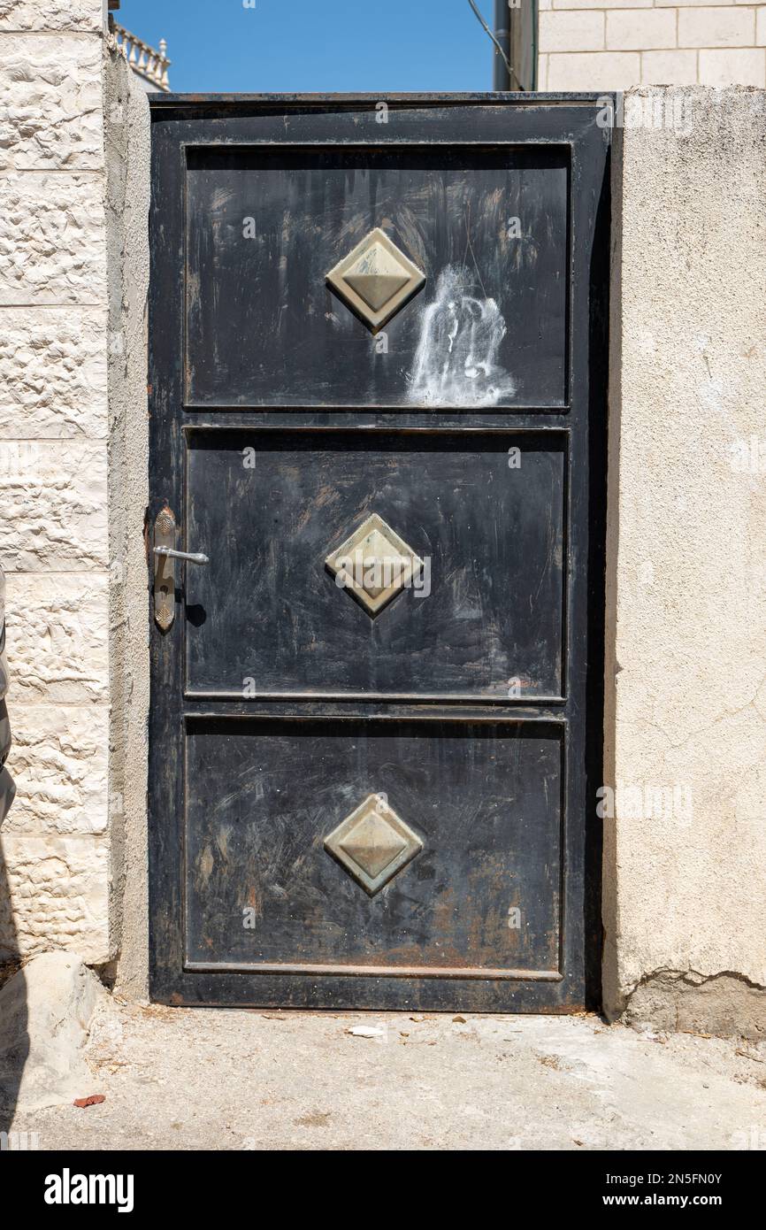 Bethlehem, West Bank, Palestine - 22 July 2022: Black Metal Door with Silver Metal Ornaments Between White Stone Walls Stock Photo