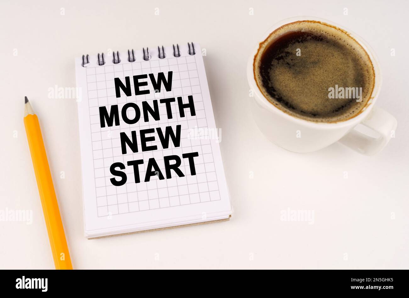 Business concept. On a white surface, a cup of coffee, a pencil and a notepad with the inscription - NEW MONTH NEW START Stock Photo