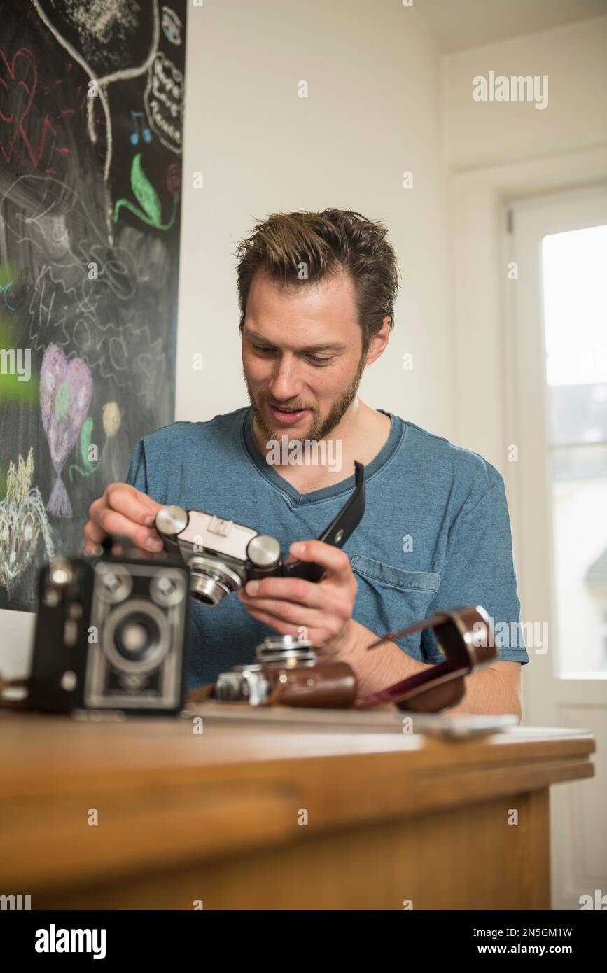 Man repairing antique camera in dining room, Munich, Bavaria, Germany Stock Photo