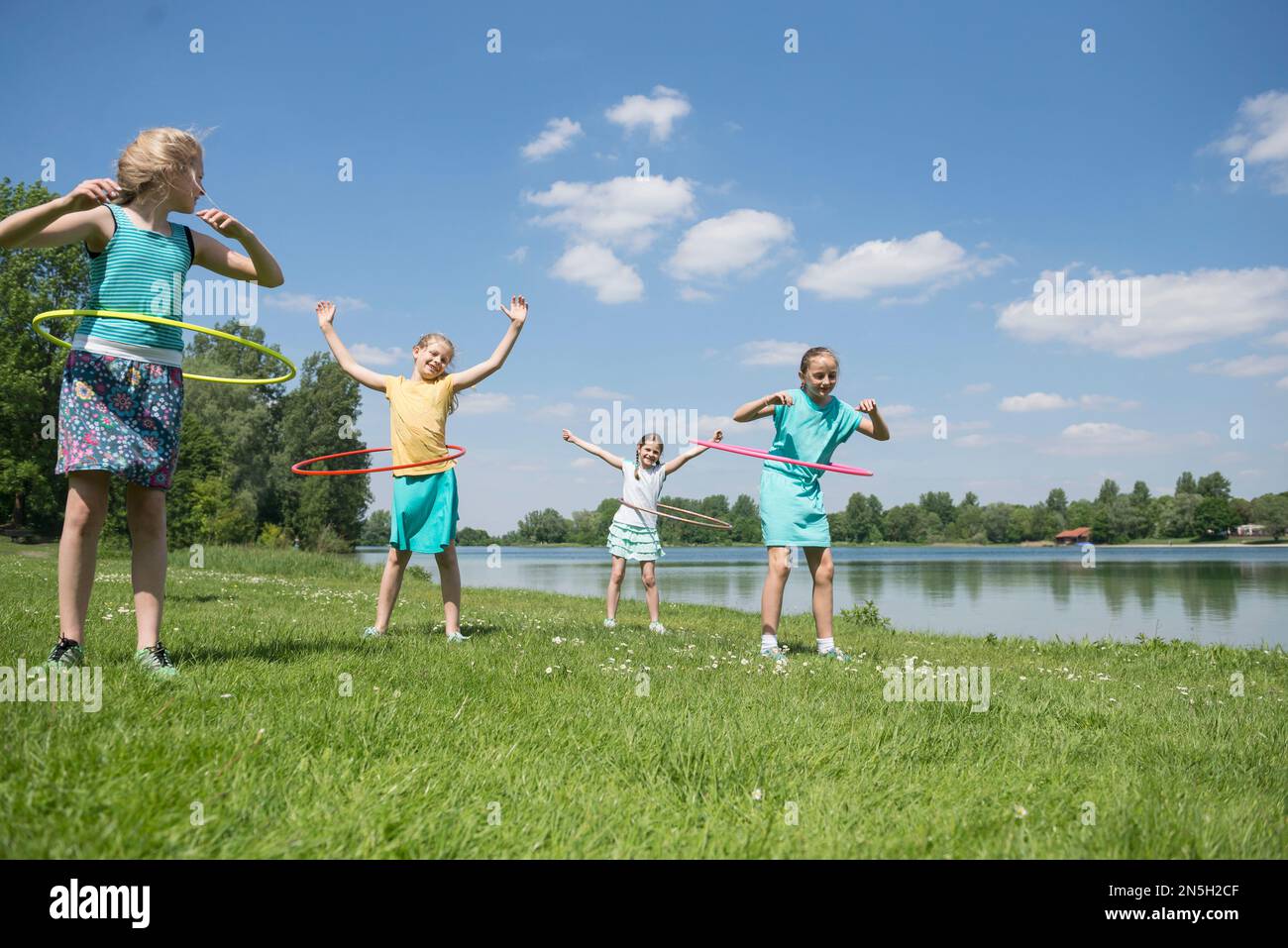 Group of friends spinning plastic hoops at lakeside, Munich, Bavaria, Germany Stock Photo