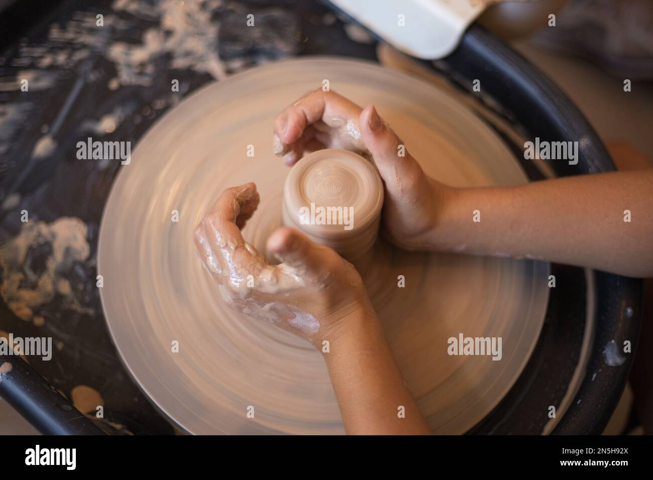 Hands of little girl creating mug on potter's wheel. Pottery wor Stock Photo