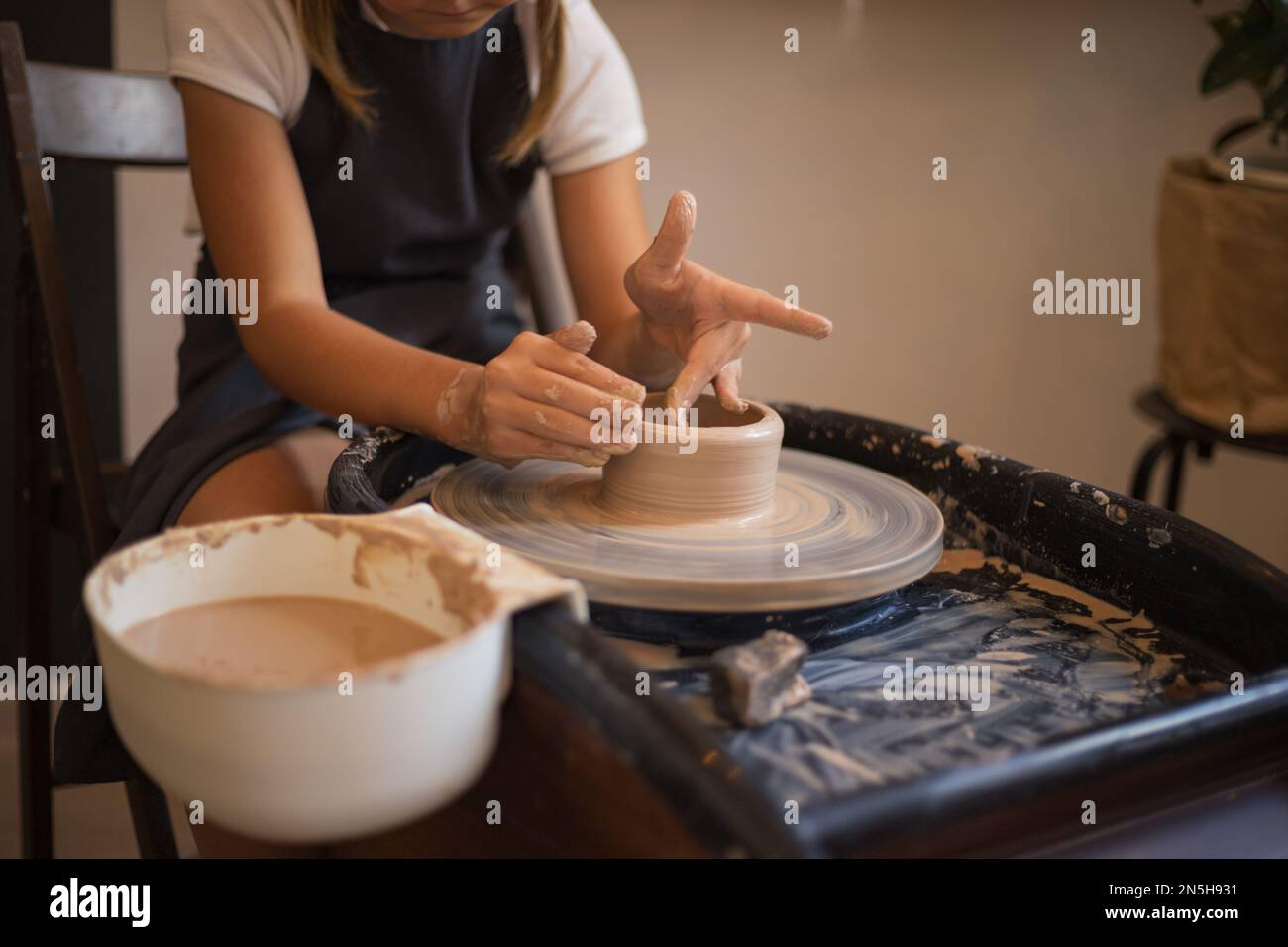 Hands of girl sculpt mug with ceramic clay on potter's wheel. Ha Stock Photo