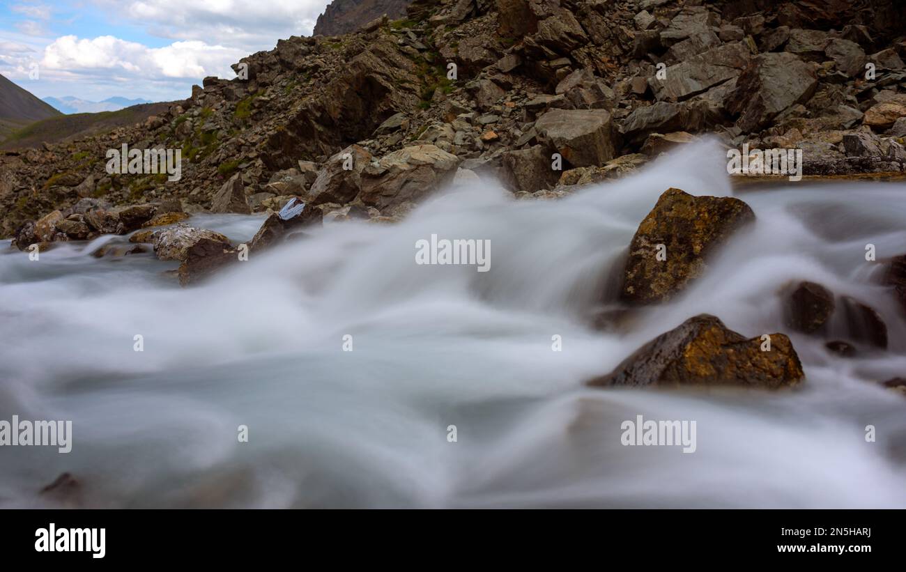 Streams of water shot at a long exposure flow among the stones in the mountains of Altai. Stock Photo