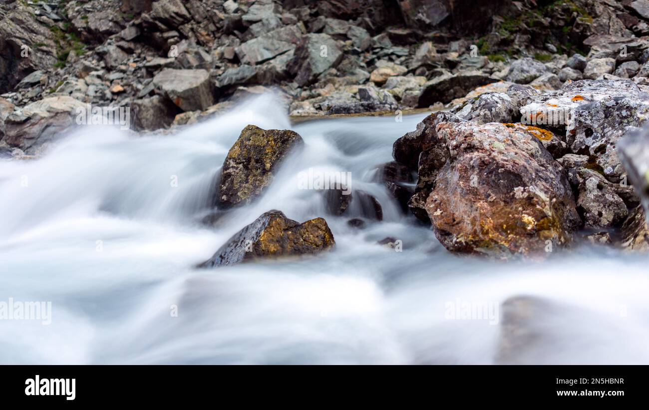 Streams of water shot at a long exposure flow among the stones of the rocks in the mountains of Altai. Stock Photo