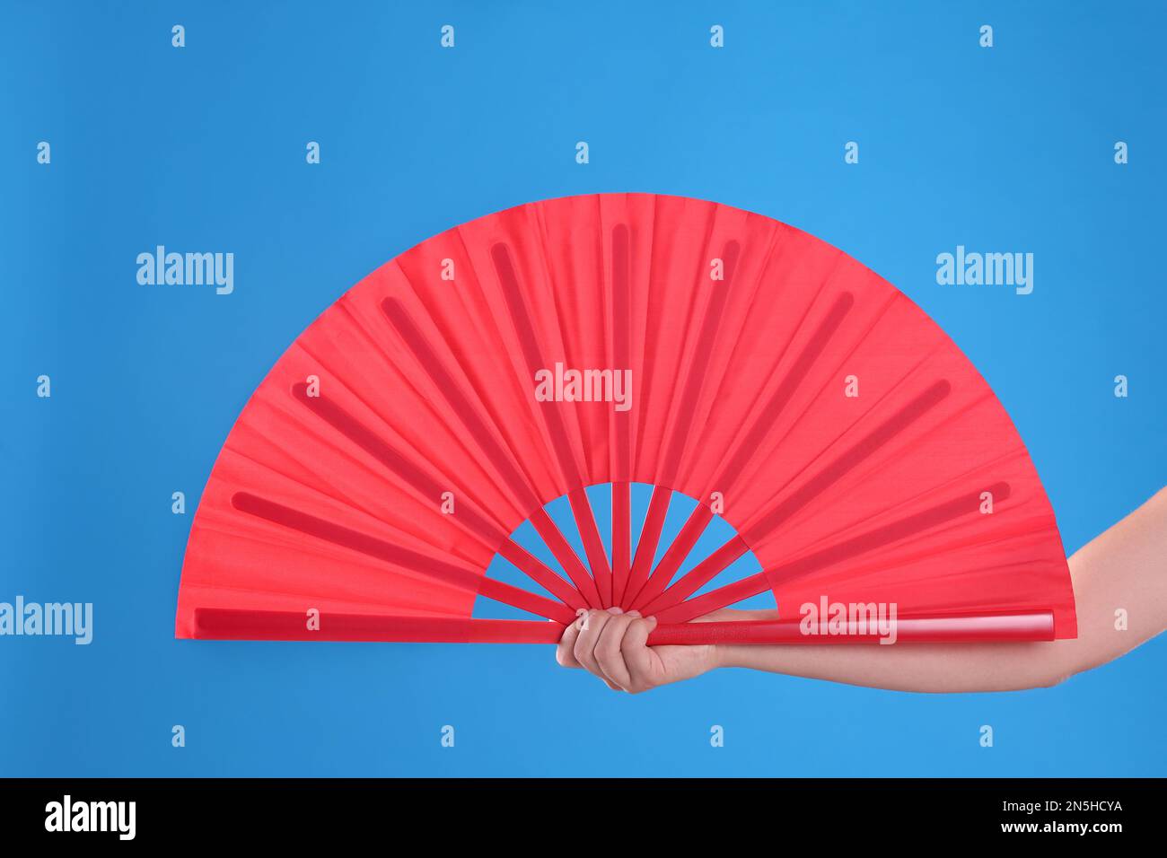 Woman holding red hand fan on light blue background, closeup Stock