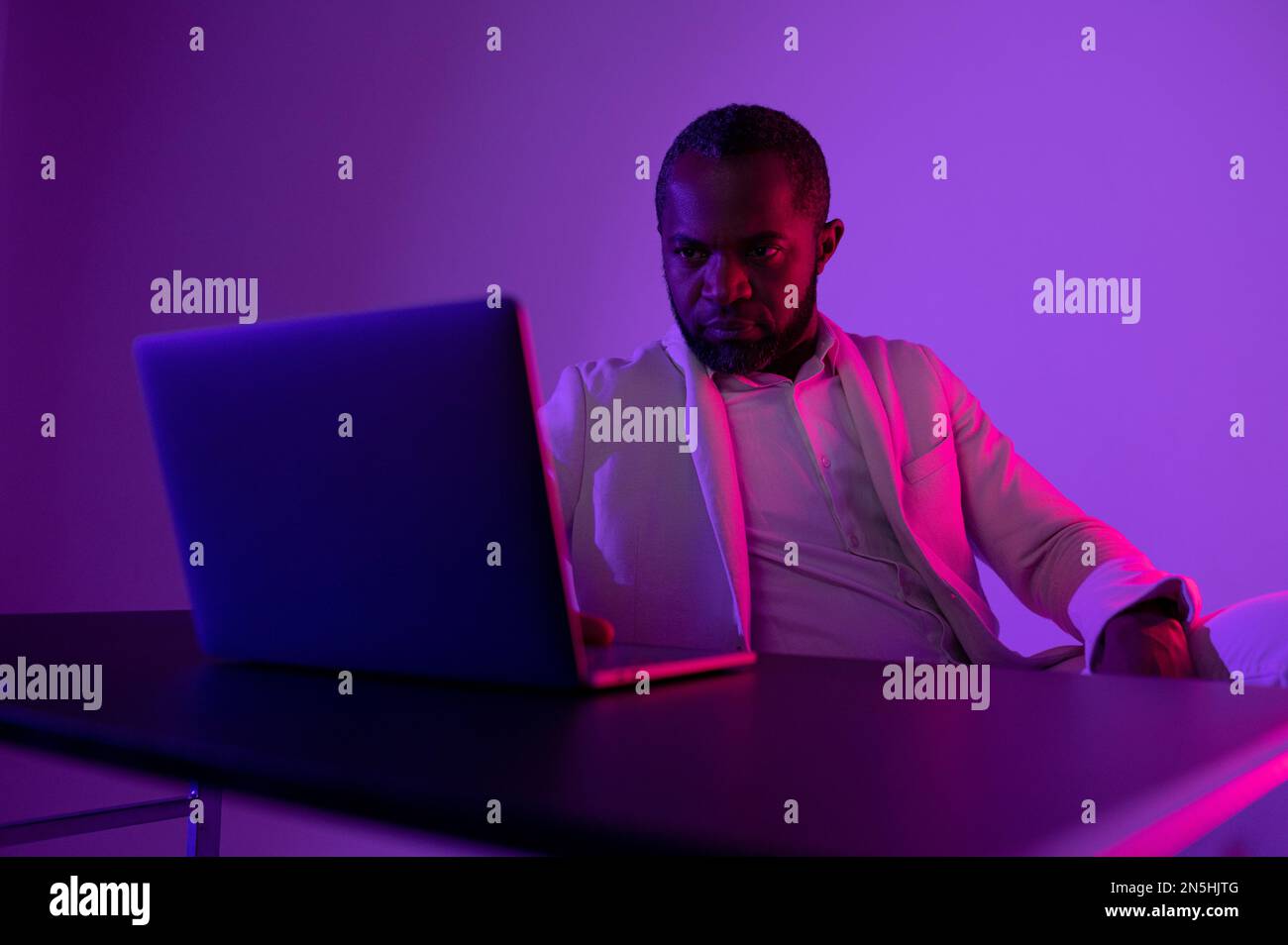 a black man in a white suit works at a computer. evening work in the office Stock Photo
