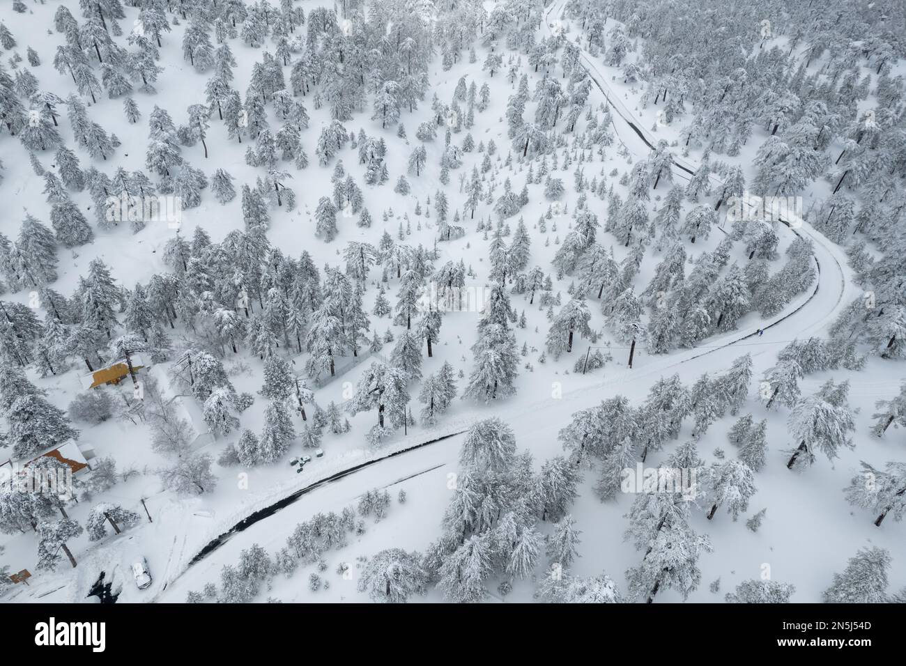 Drone aerial of a frozen dangerous road crossing a snowy forest ...