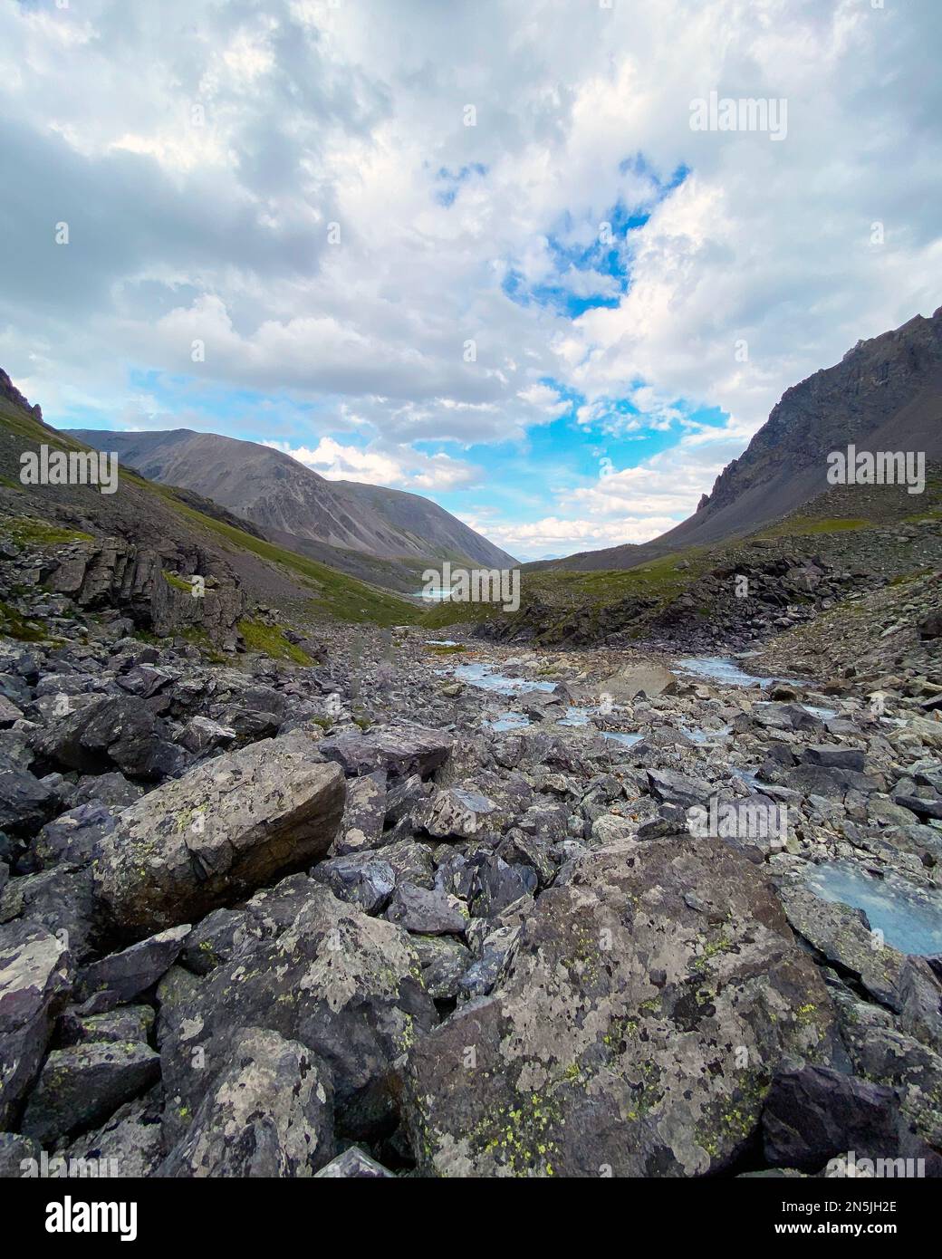 The water of a fast-flowing alpine stream among stones flows to a lake in the Altai Mountains in Siberia. Vertical frame. Stock Photo