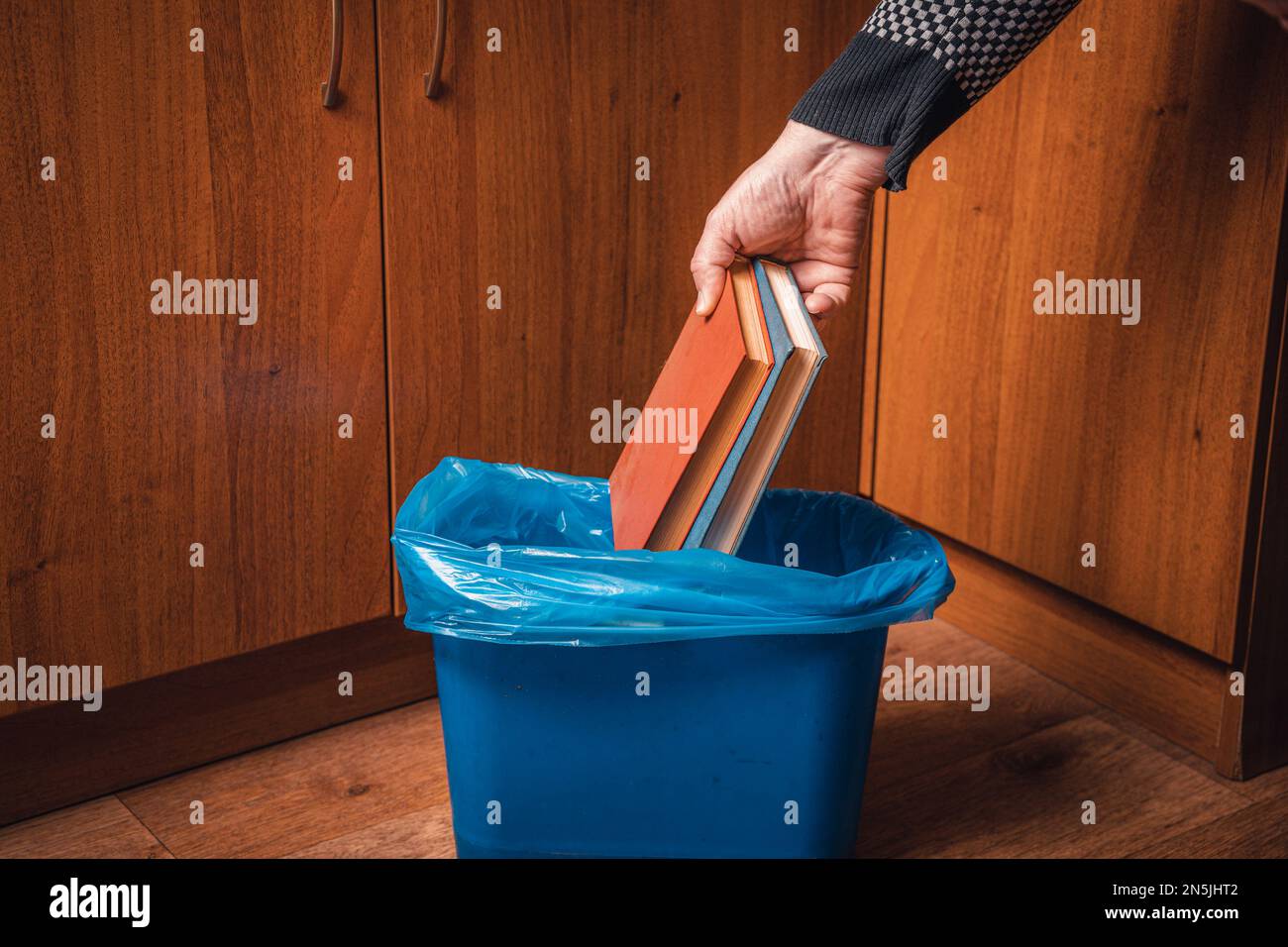 A man throws paper books into a trash can. Man's hand with old books