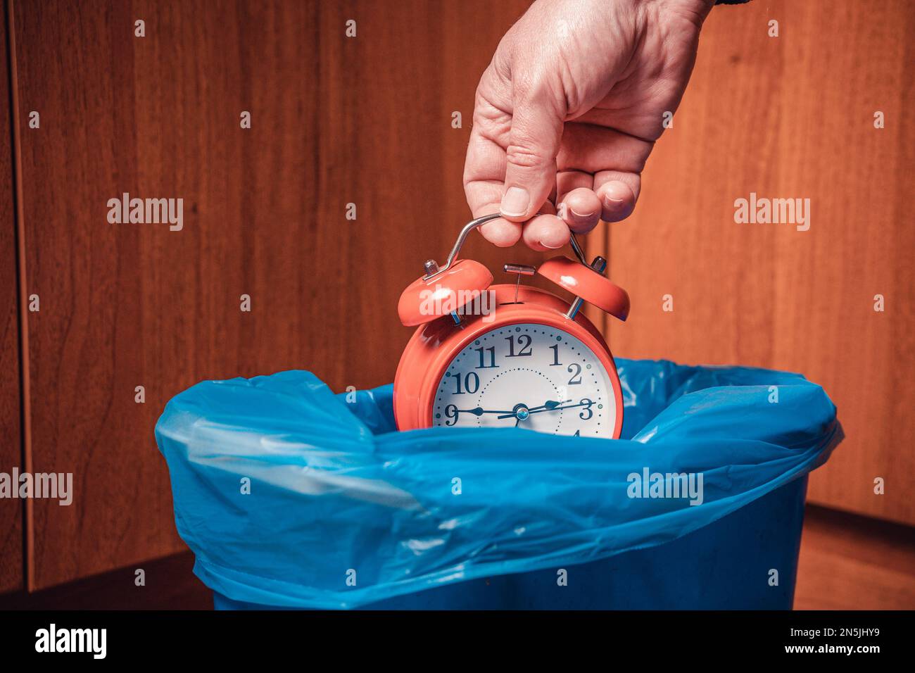The man throws the alarm clock in the trash. Man's hand with a red