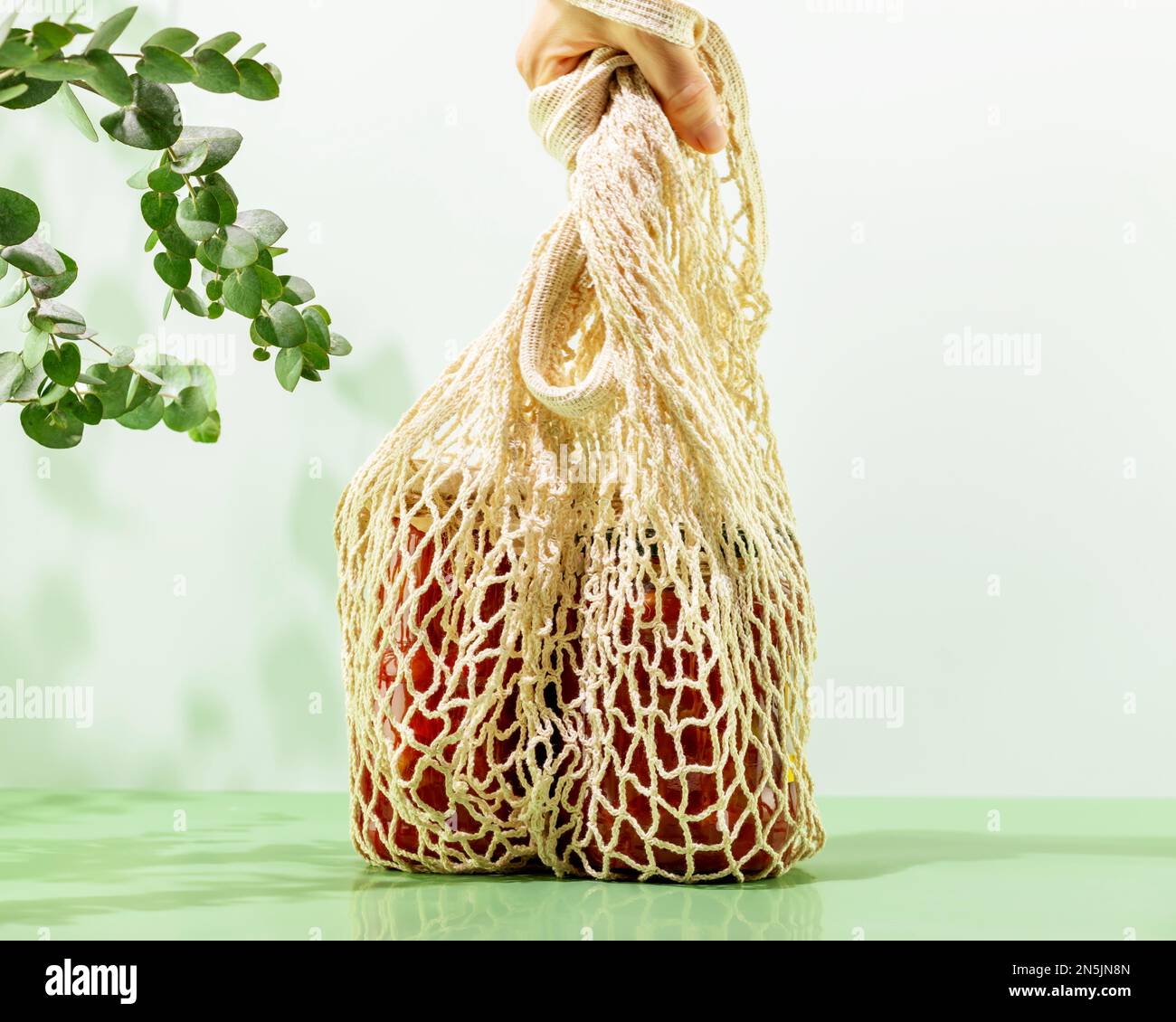 Hand is holding mesh shopping bag with glass bottles with fermented