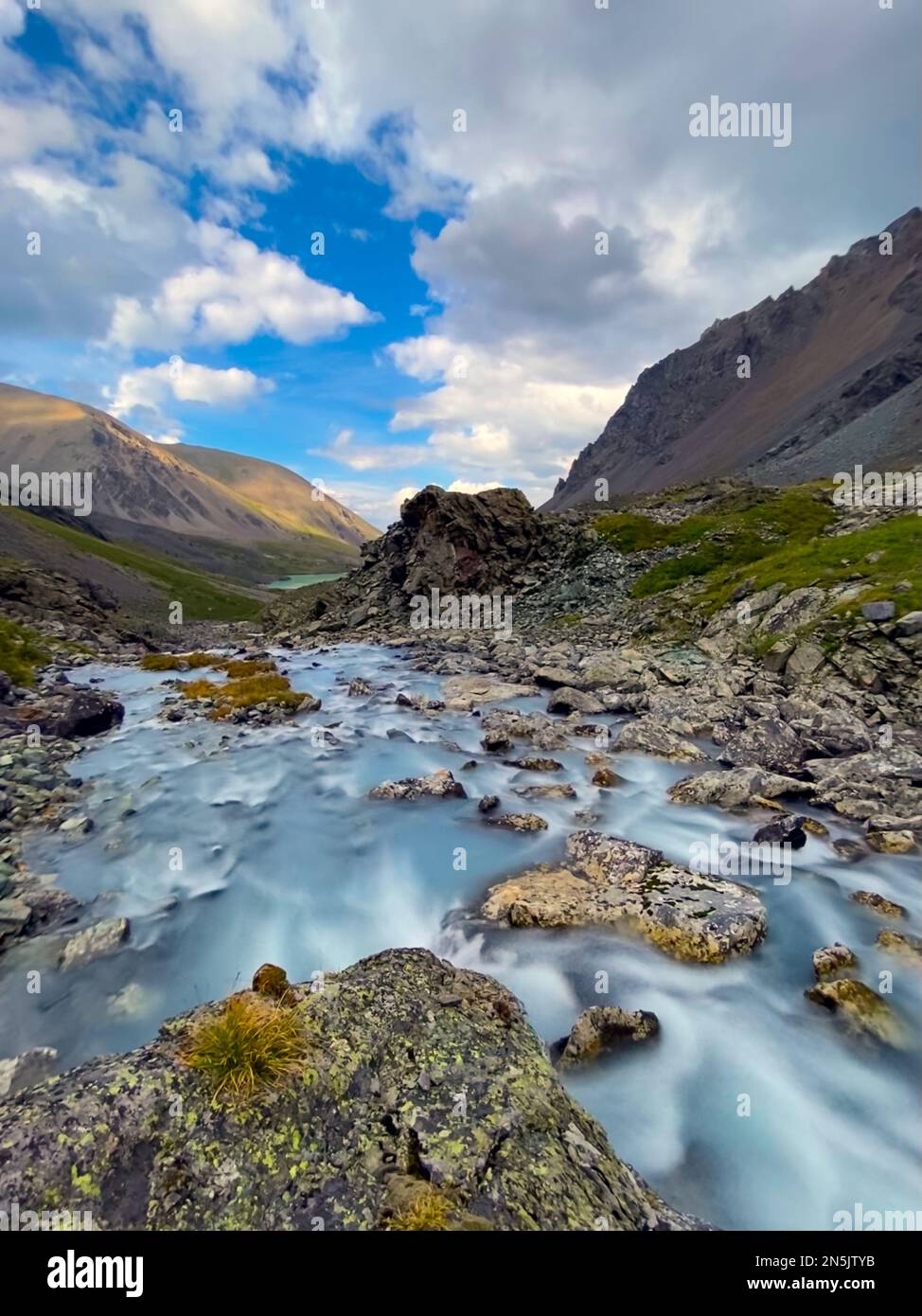 The water of a fast-flowing alpine stream among stones flows to a lake in the Altai Mountains in Siberia. Vertical frame. Stock Photo