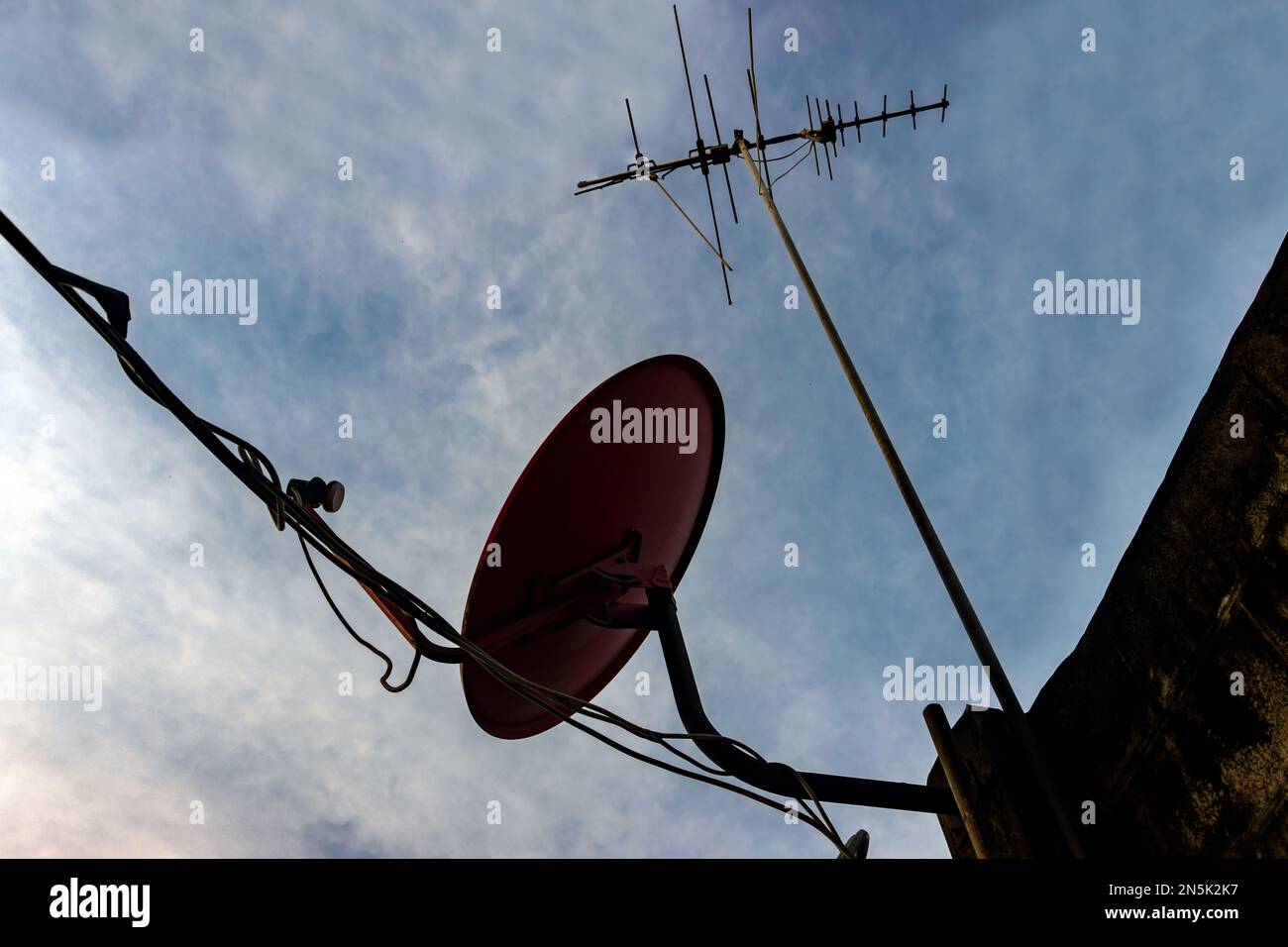 Silhouette of antenna and satellite dish attached to wall with early evening sky Stock Photo