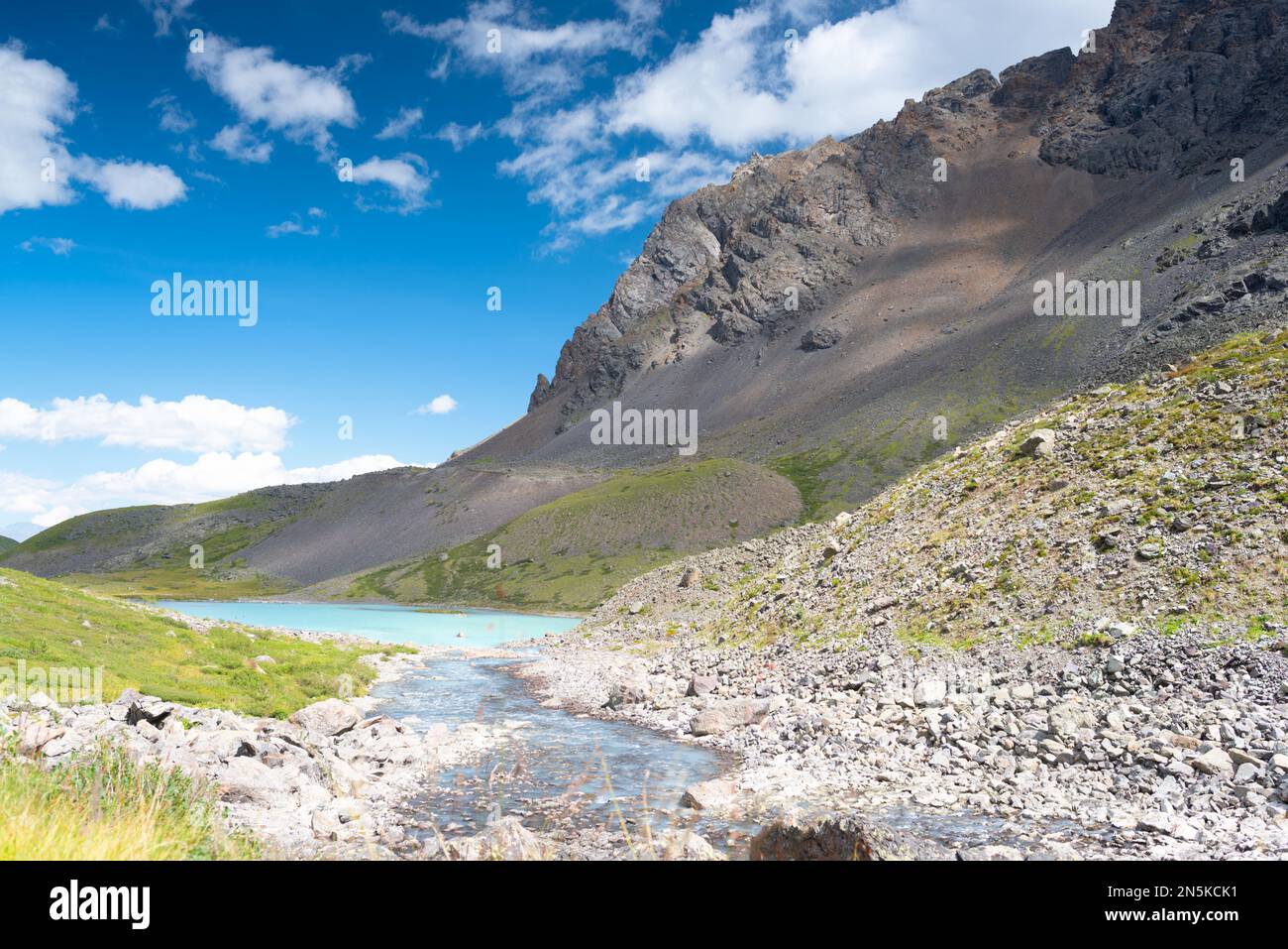Alpine lake among rocks of stones and shores with green grass during the day in the Altai mountains in Siberia. Stock Photo