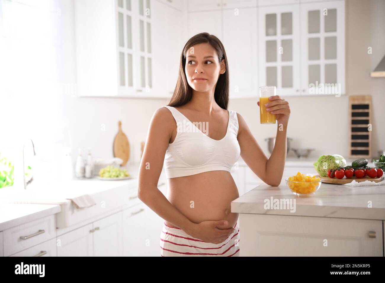 Young pregnant woman with glass of juice in kitchen. Taking care of baby health Stock Photo