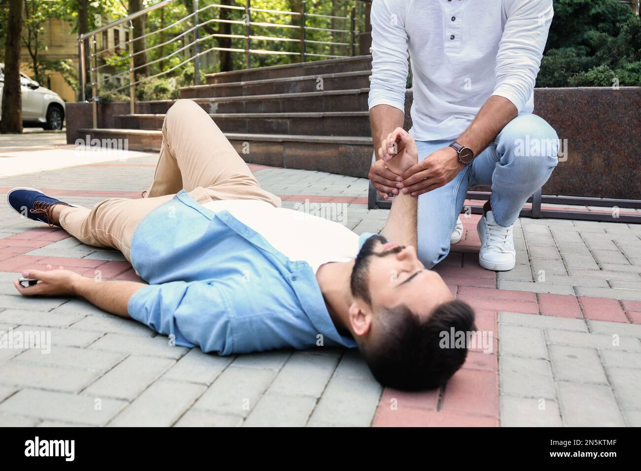 Passerby checking pulse of unconscious young man on city street. First ...