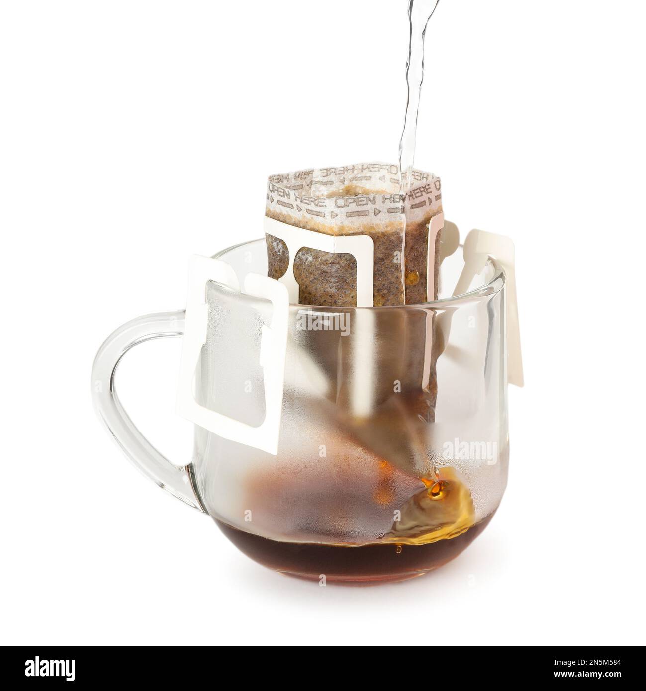 Pouring hot water into glass cup with drip coffee bag isolated on white