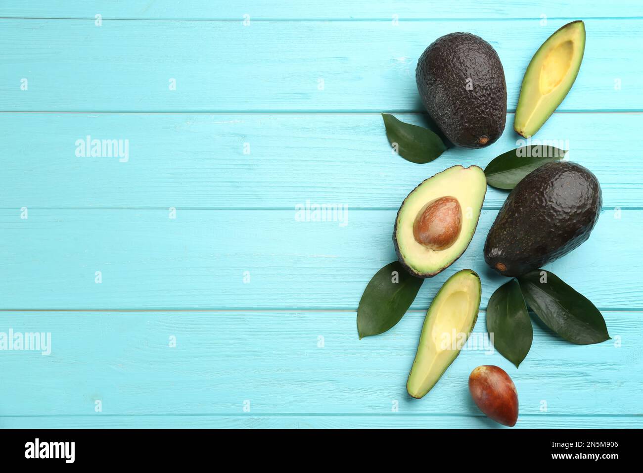 Whole and cut avocados with green leaves on turquoise wooden table ...