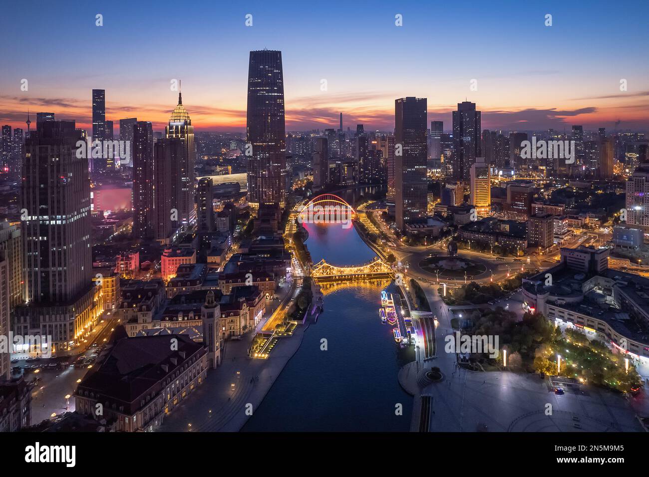 A drone modern cityscape view with a river and illuminated buildings at ...
