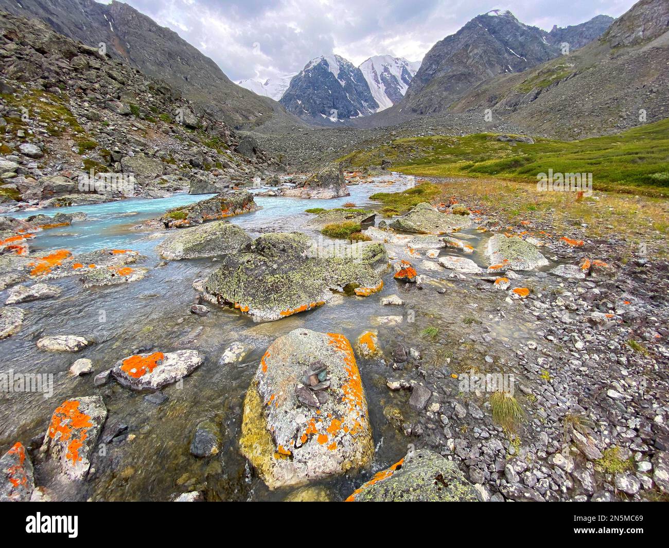 Alpine stream flows among the orange stones from the mountains with glaciers in the Altai in Siberia. Stock Photo