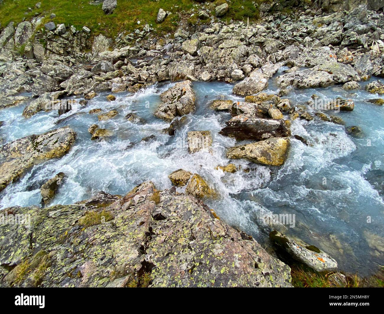 The water of a fast-flowing alpine stream among the stones of rocks with green lichen in the Altai mountains in Siberia. Stock Photo