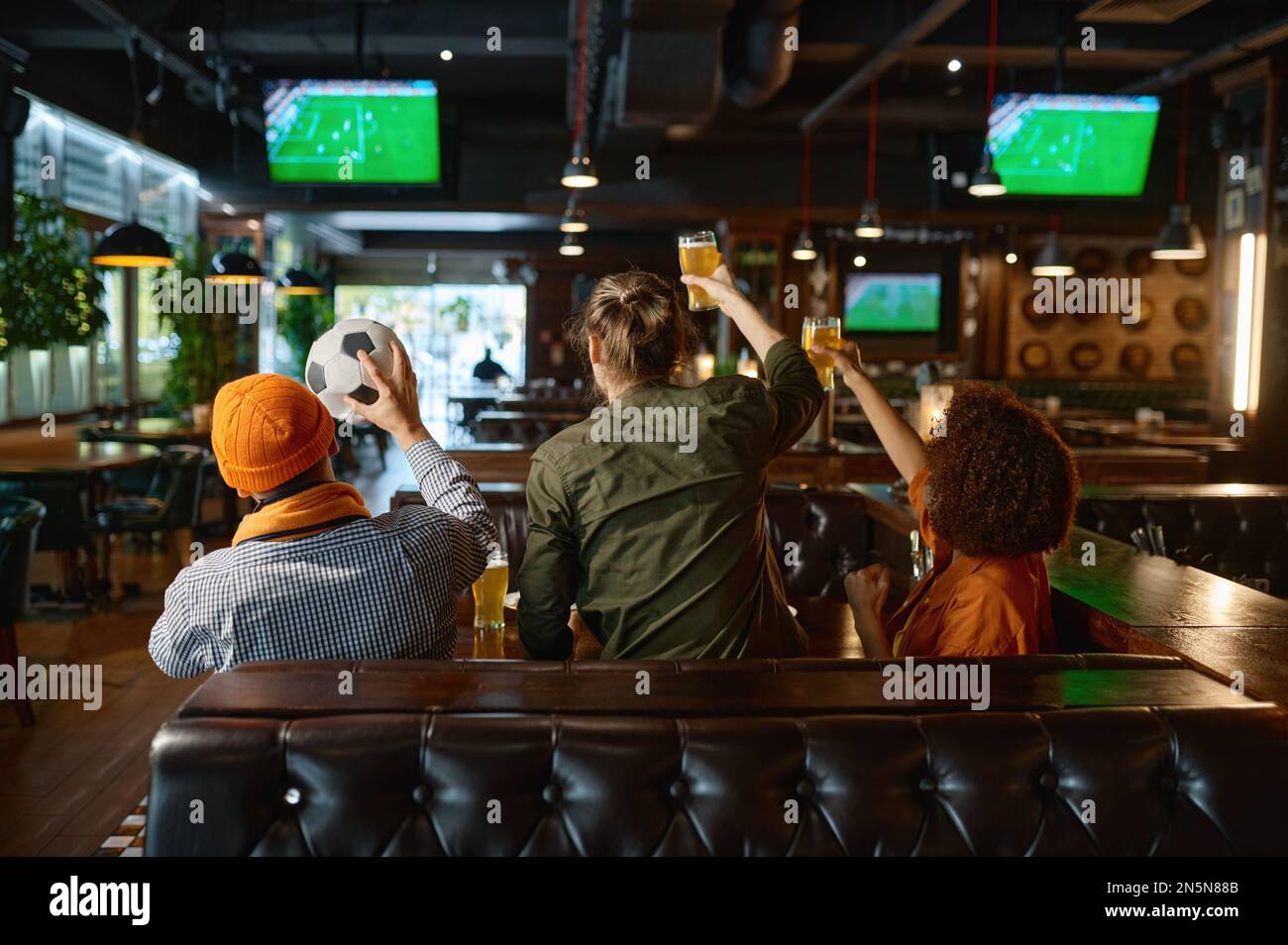 Group of young friends watching football on tv screen at sports bar