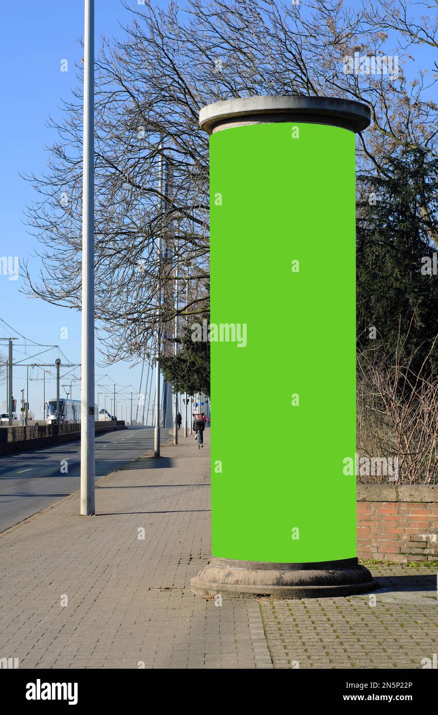 Empty advertising pillar on a street with green free copy space, promotion mock up. Blank advertising panel with unidentifiable persons Stock Photo