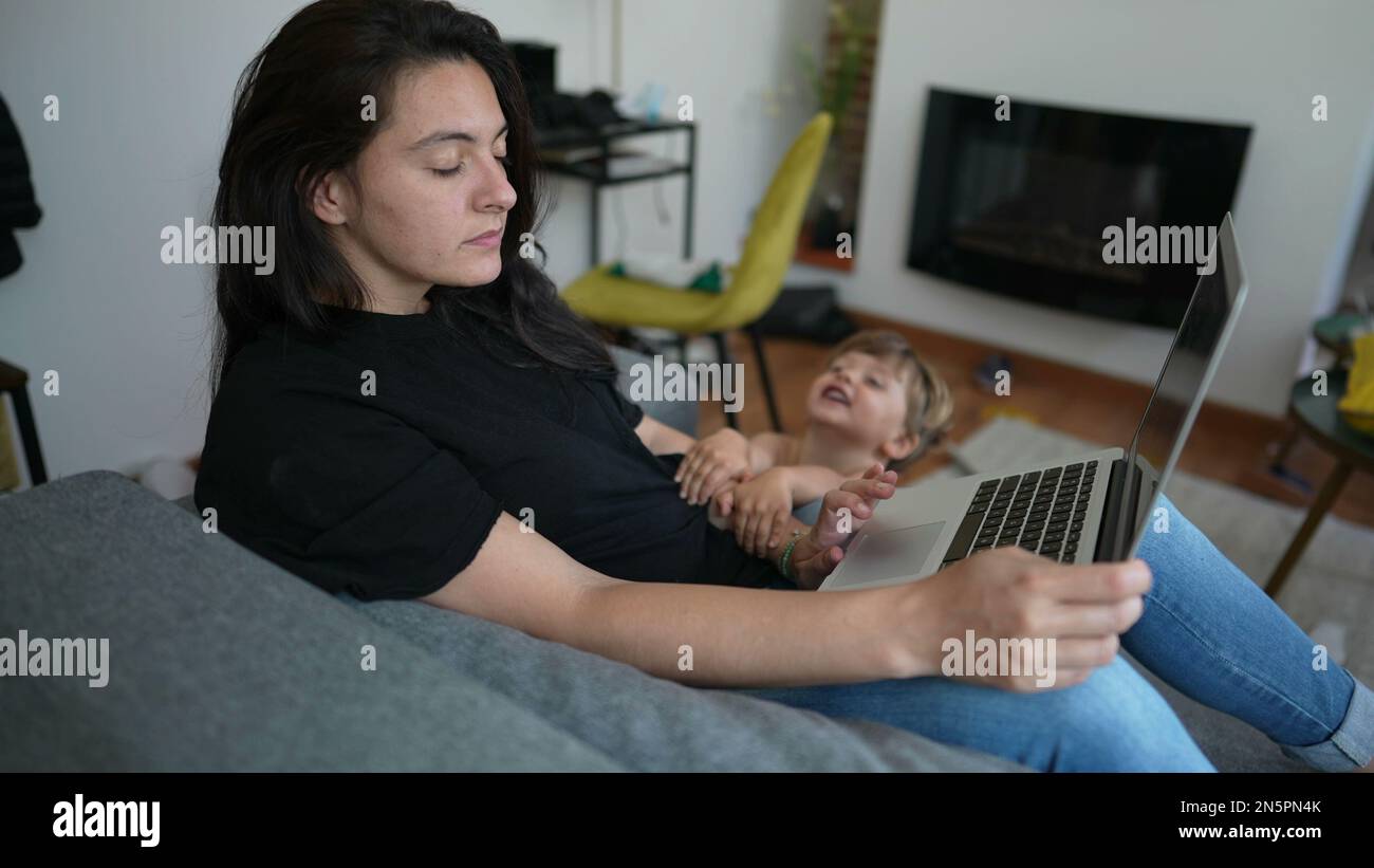 Child interrupting mother working from home in front of laptop. Parent ...