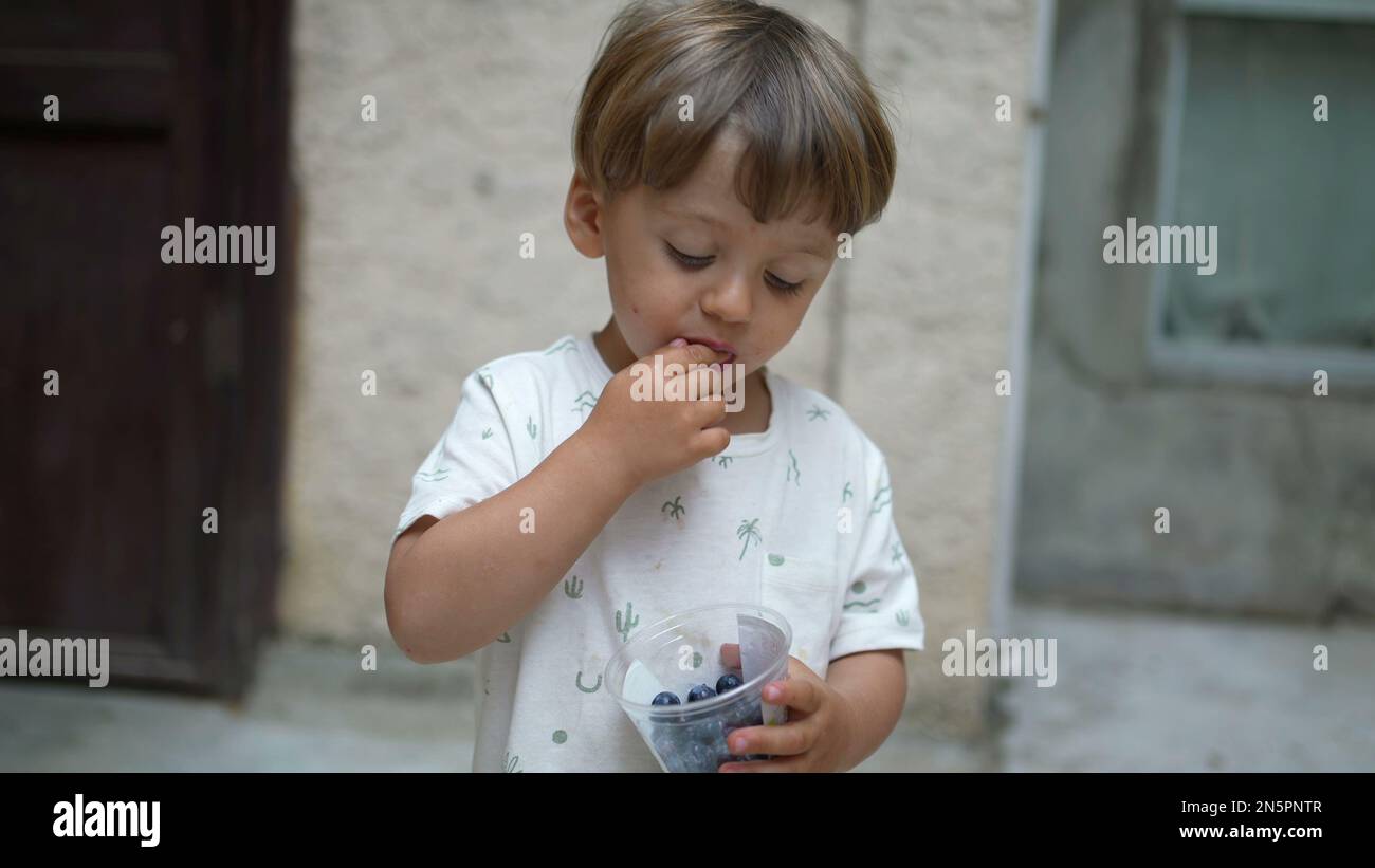 One little boy eating blueberries. Child standing outside snacking healthy fruit. kid eats