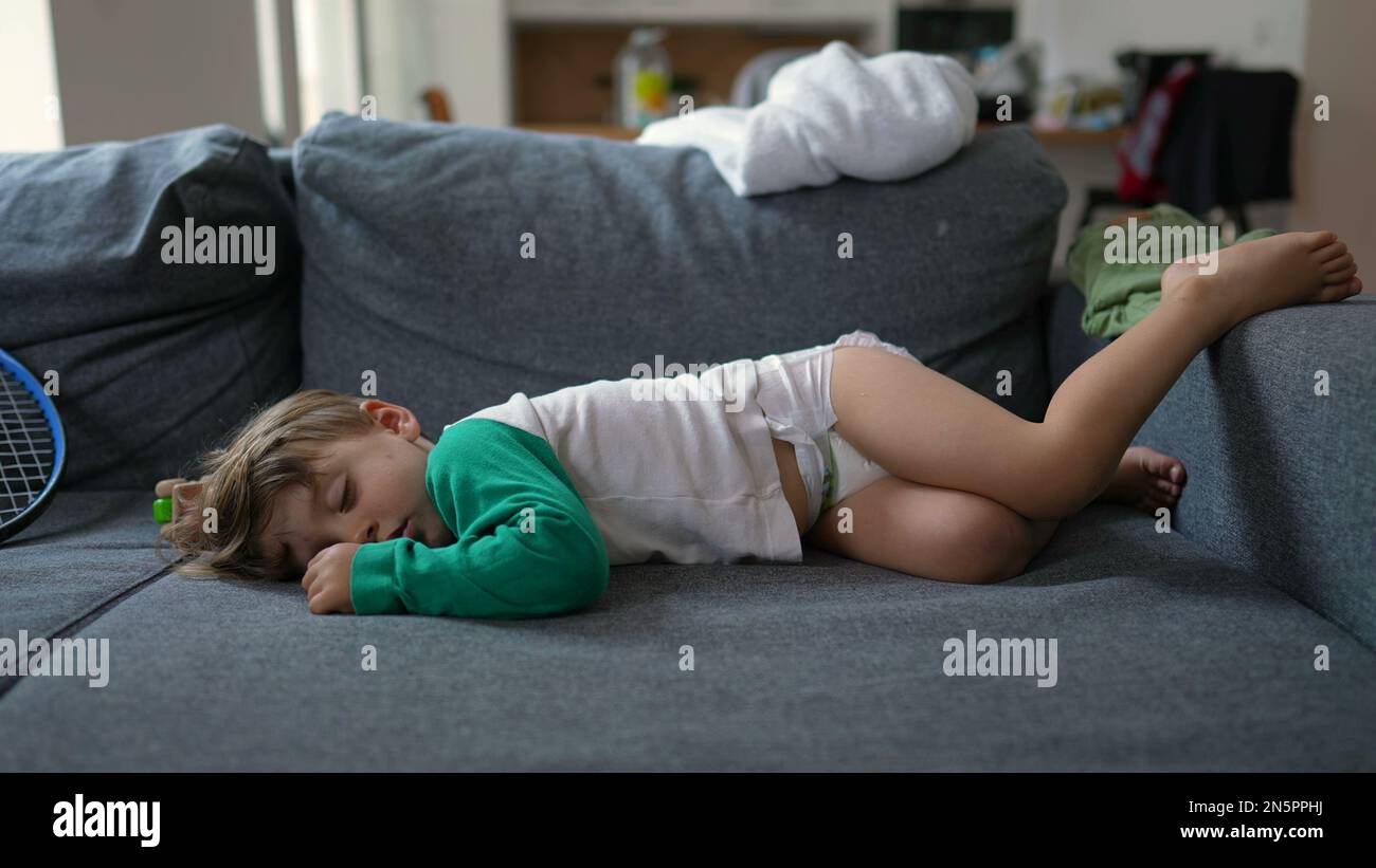 Funny little boy laying on sofa sleeping during afternoon nap. Baby toddler wearing diapers