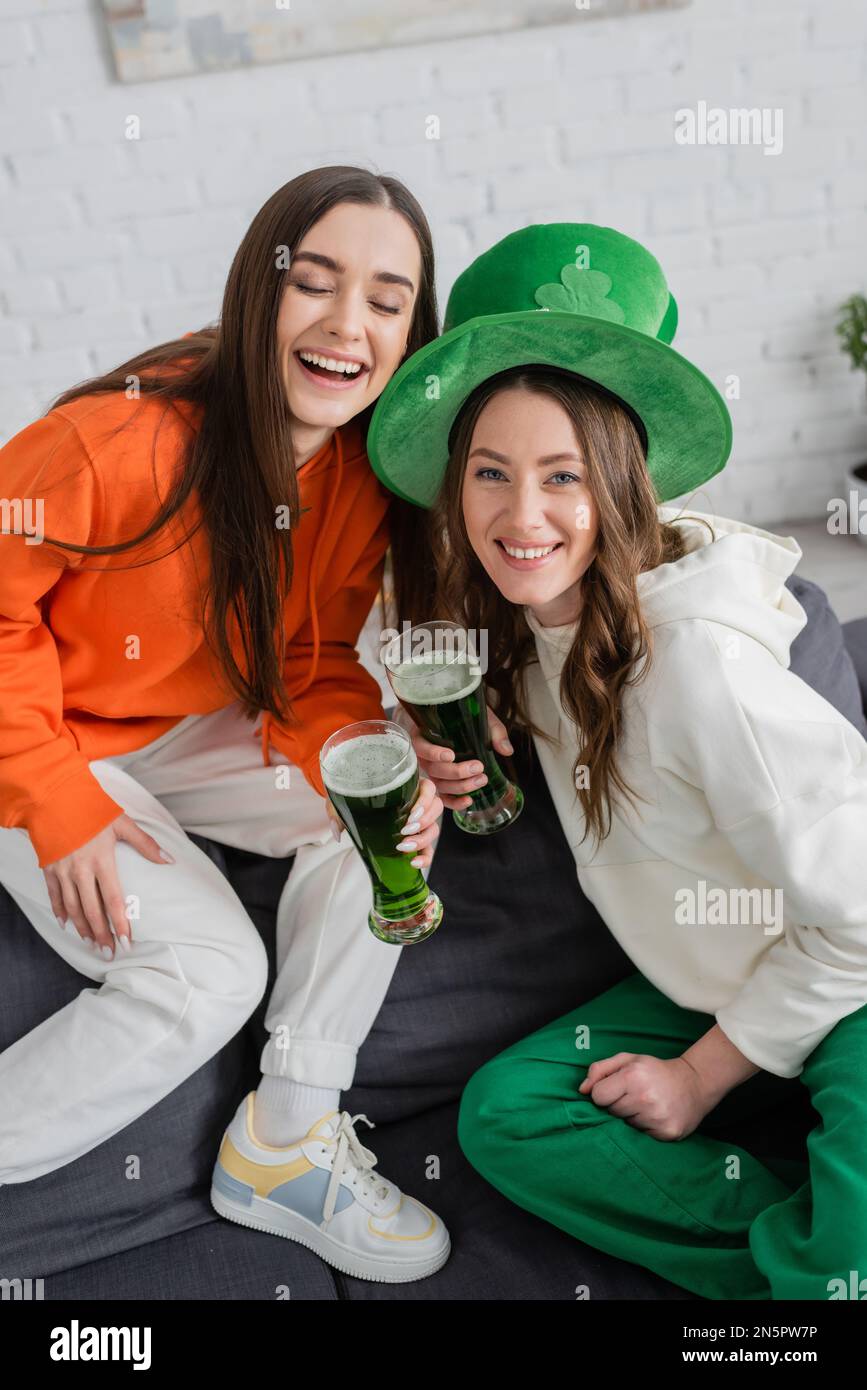 Positive young women holding green beer during saint patrick celebration at home Stock Photo