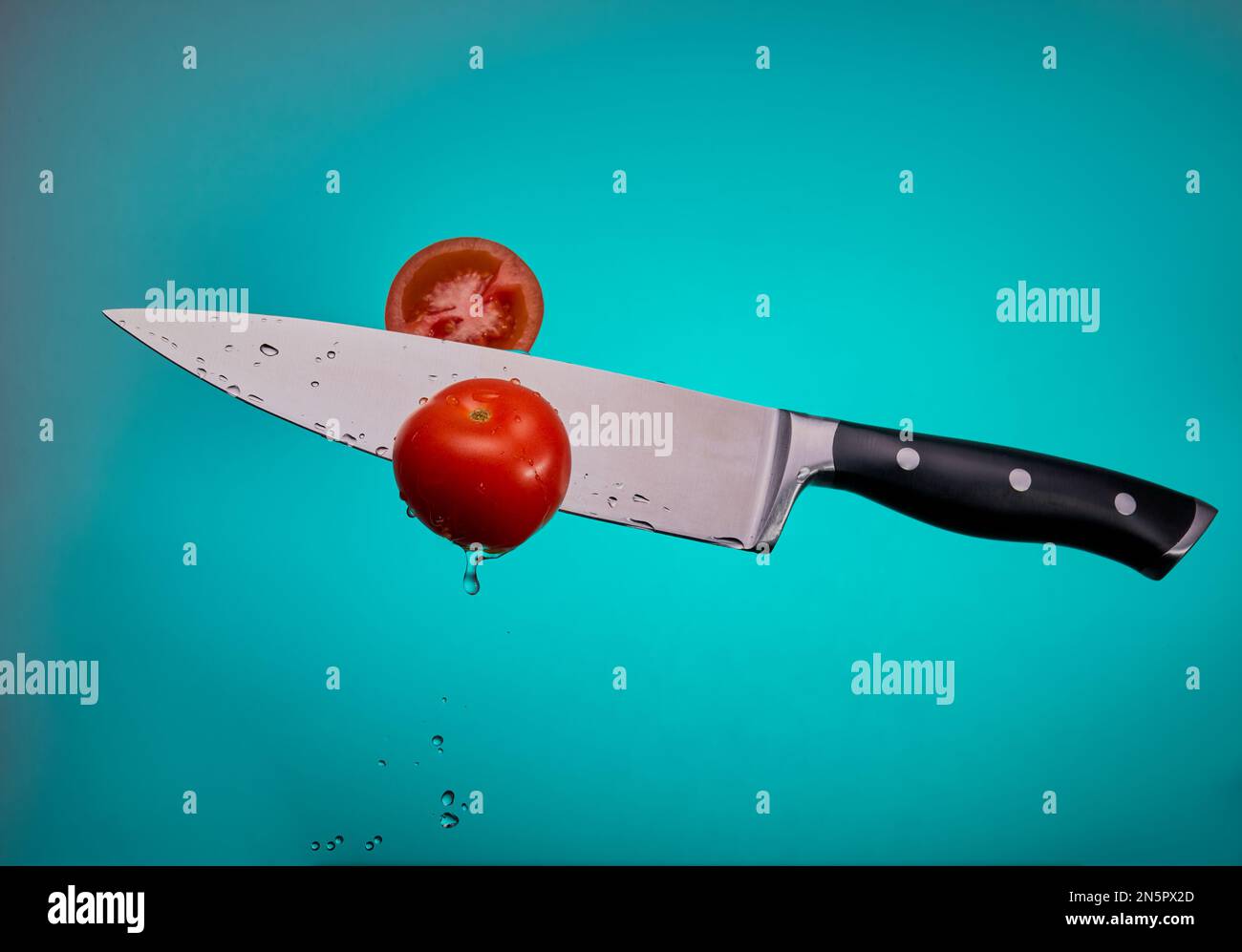 Flying chef's knife cutting threw tomatoes isolated on a blue gradient