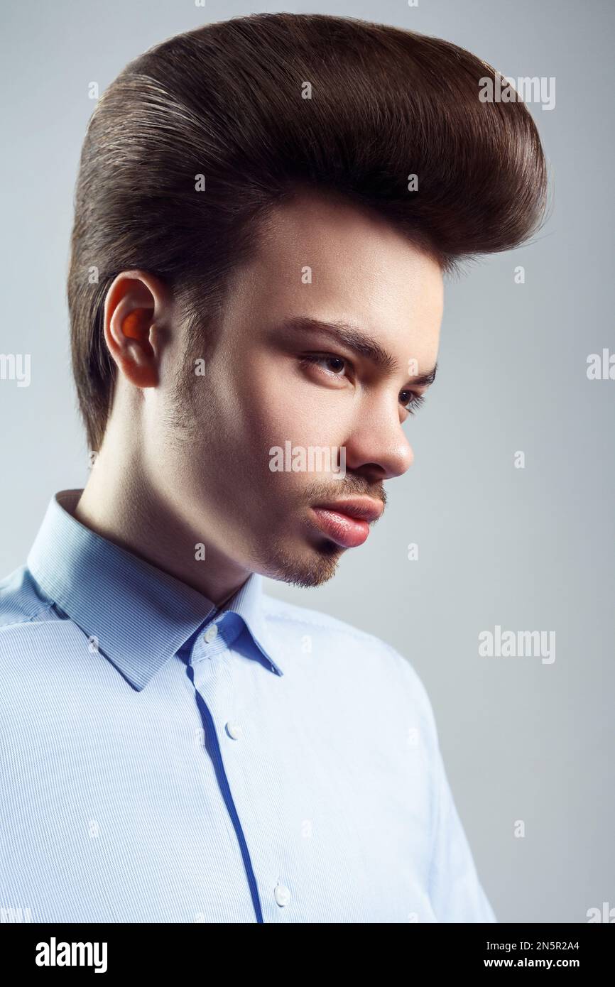 Side view portrait of handsome confident man with mustache and beard with retro classic elvis presley hairstyle, looking away, wearing blue shirt. Indoor studio shot isolated on gray background. Stock Photo