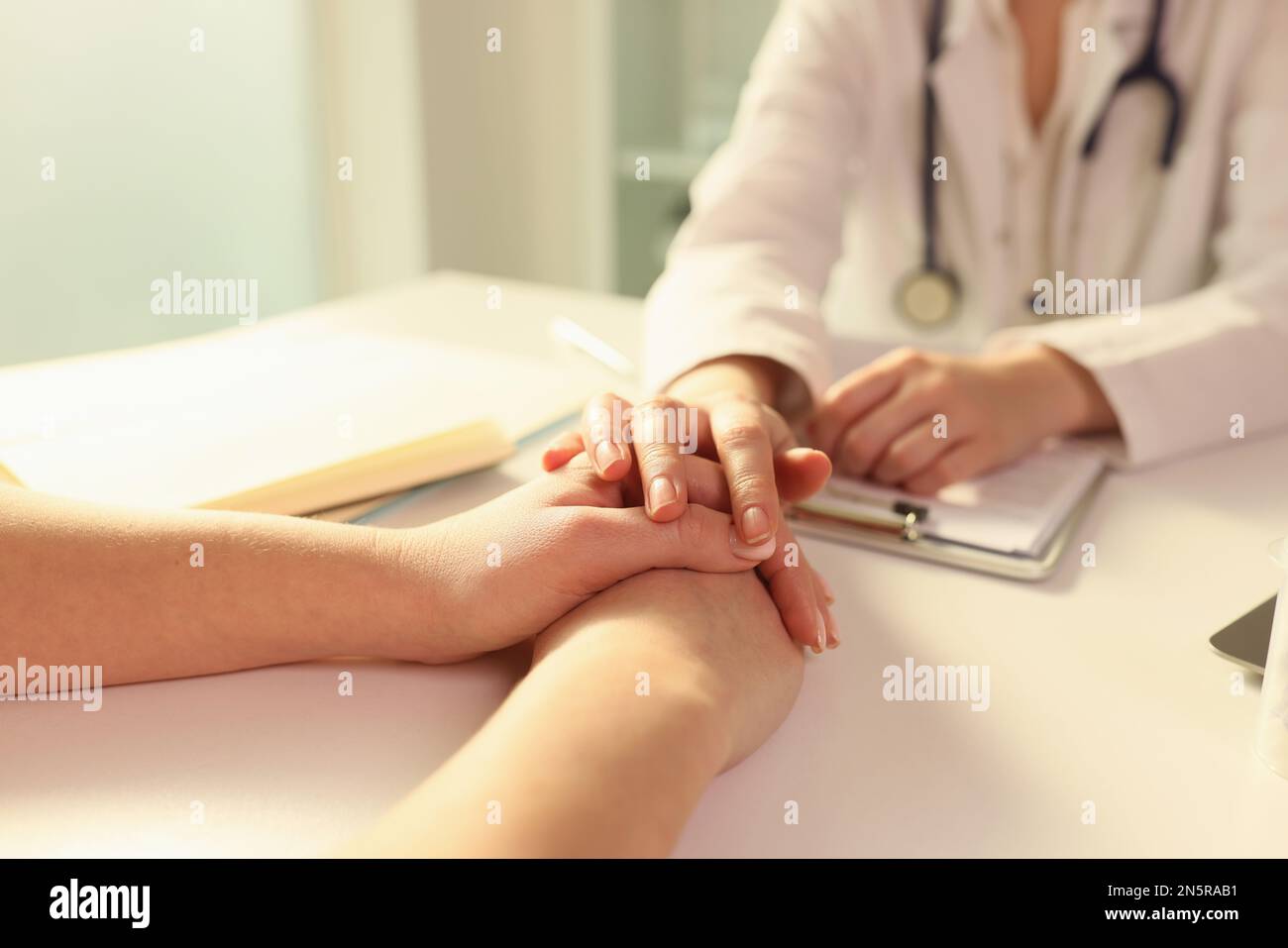 Female doctor puts her hand on hands of woman patient while explaining diagnosis. Stock Photo