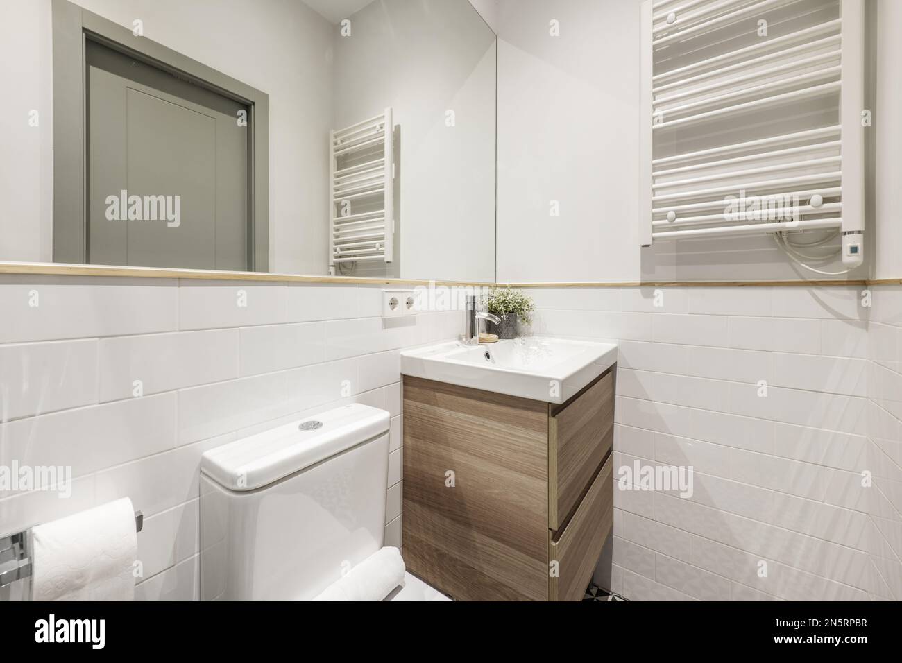 Newly renovated bathroom white porcelain sink on wooden cabinet with drawers, heated towel rail, integrated wall mirror with wooden border and decorat Stock Photo