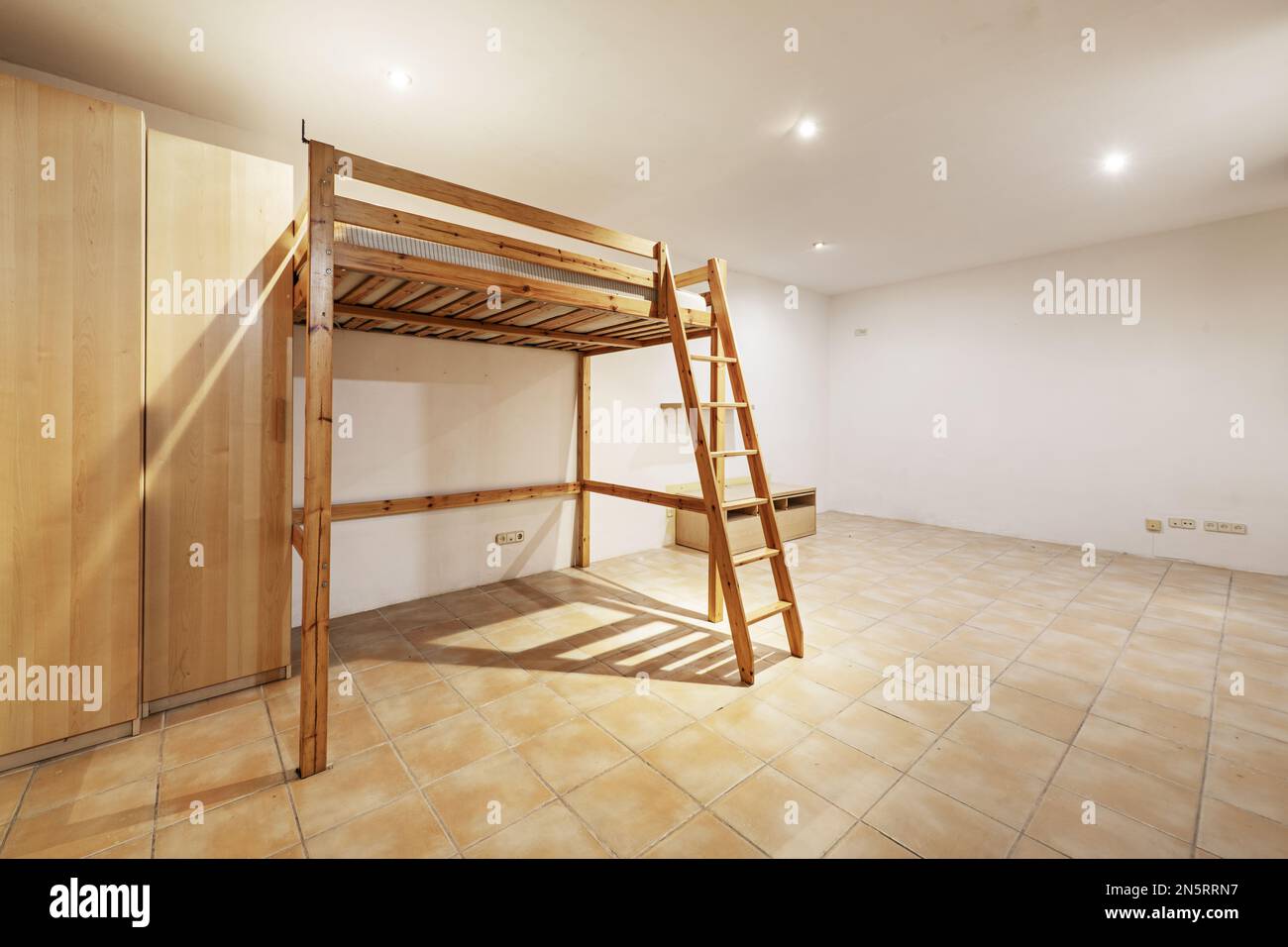 Studio apartment with a double bed on a raised wooden frame with a ladder and cupboards in one corner Stock Photo