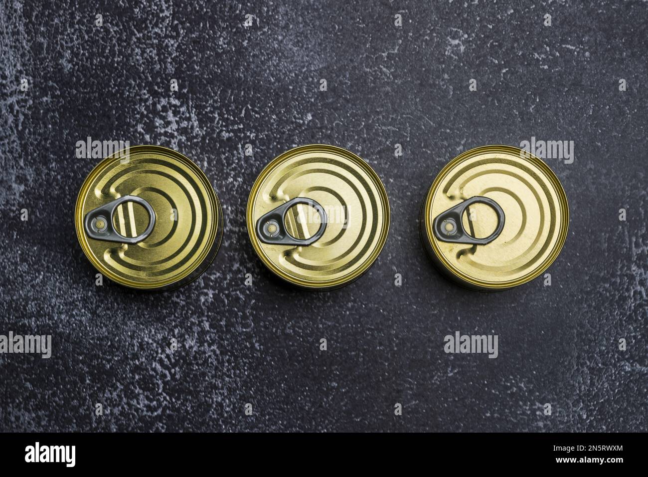 A trio of small circular ringclosed tins that are easy to open on a gray surface Stock Photo