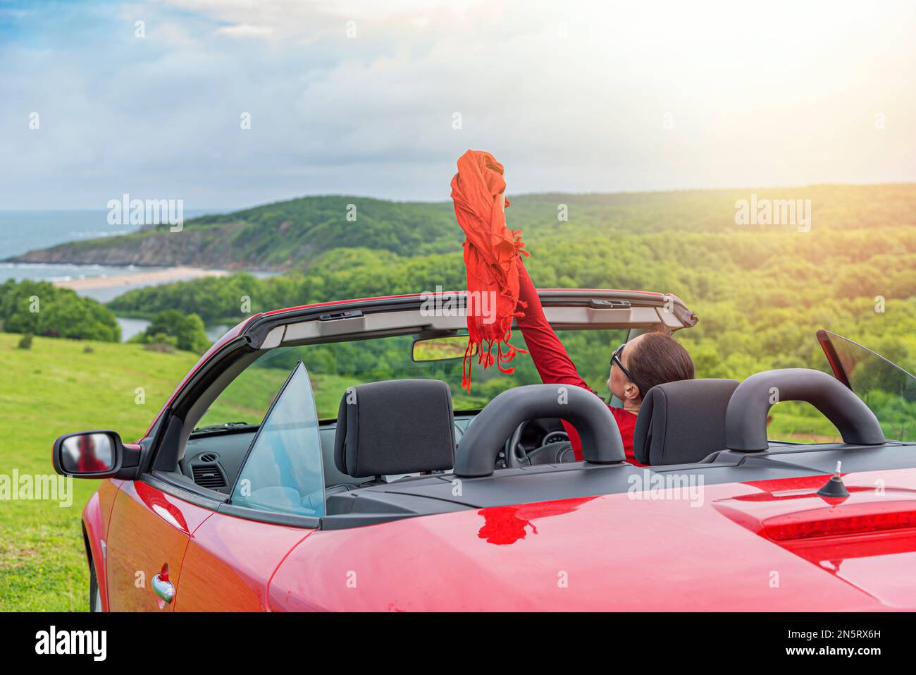 Woman in red car with open roof at background of sea water Stock Photo