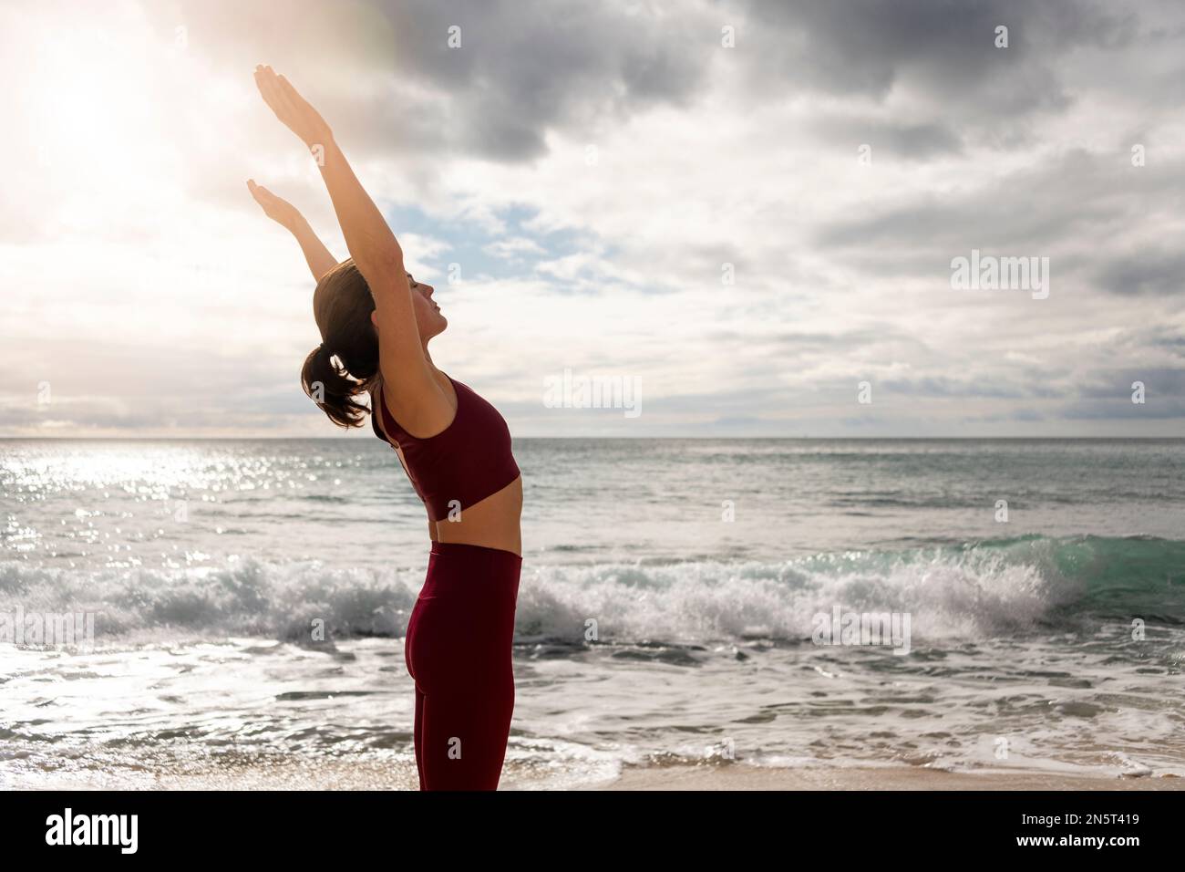 Sporty woman standing by the ocean with her arms raised. Stock Photo