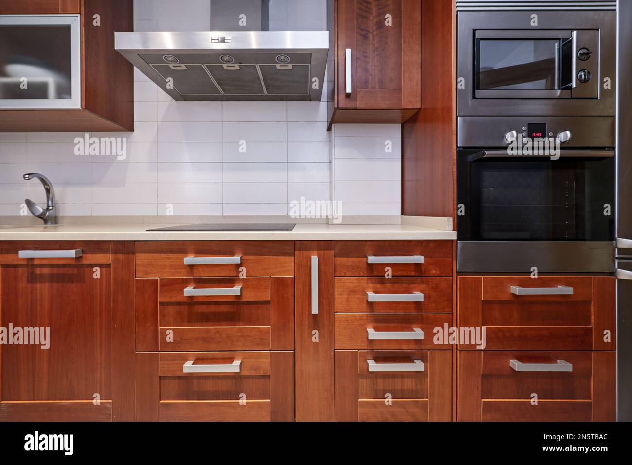 Image of the front of a kitchen with reddish wood with many metal handles and