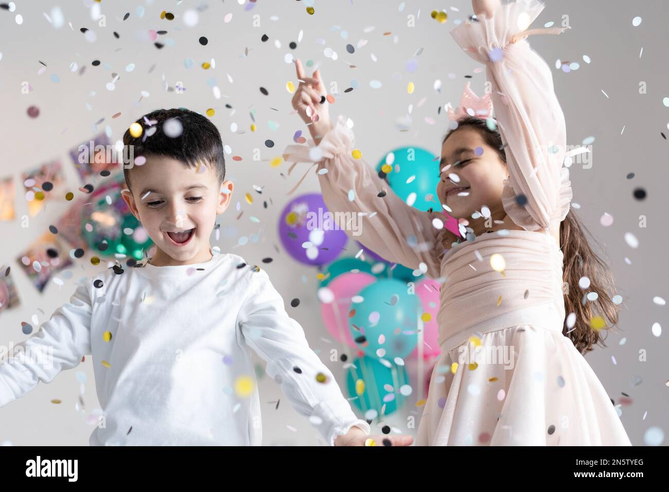 Smiling children with outstretched hands near falling confetti on party background. Stock Photo