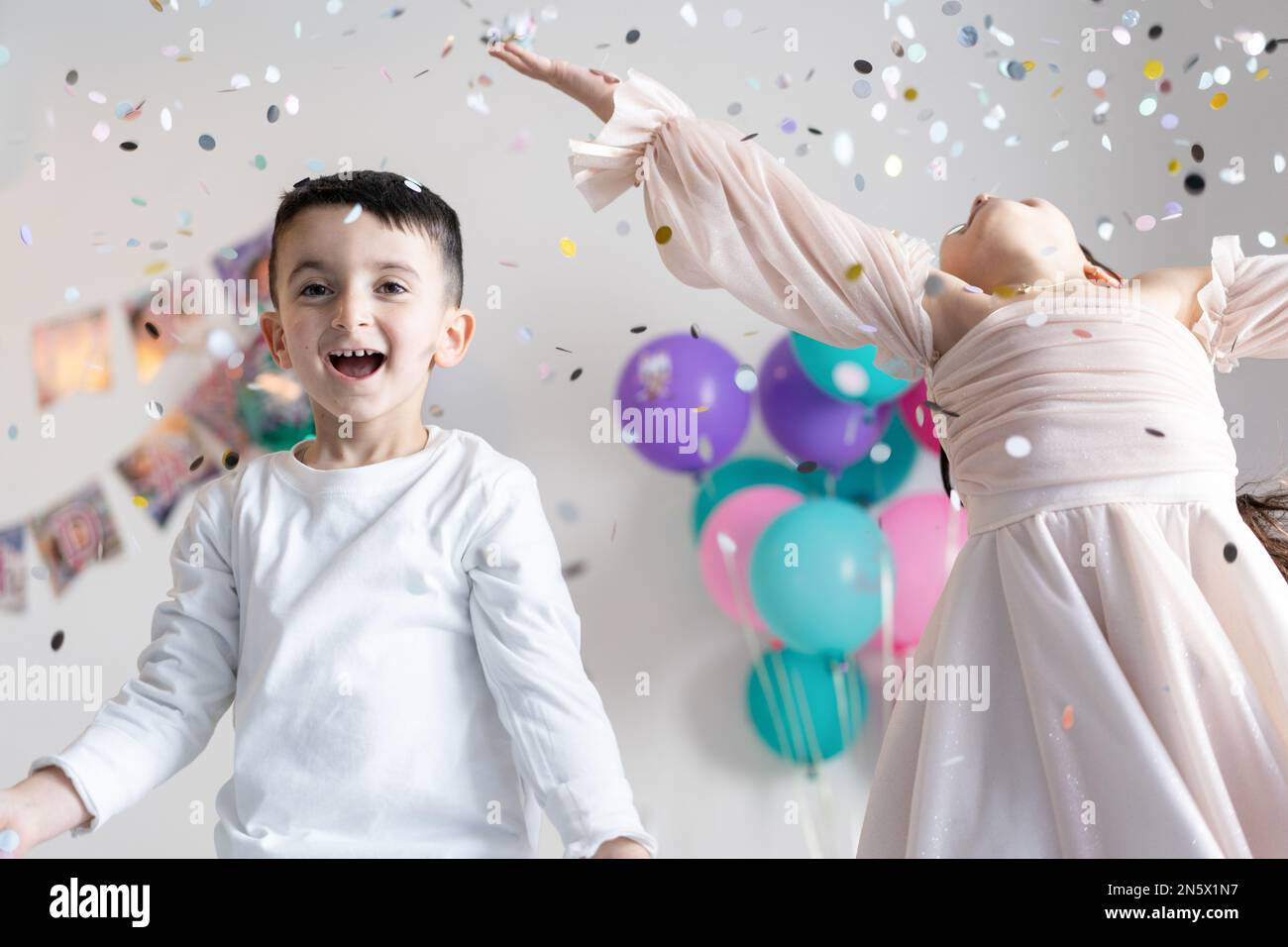 Two kids throwing colorful confetti and looking happy on birthday party. Stock Photo