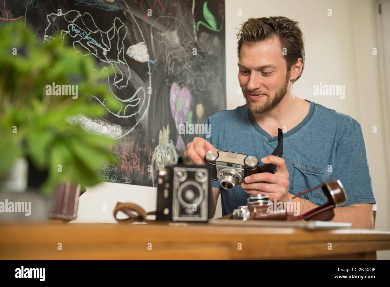Man repairing antique camera in dining room, Munich, Bavaria, Germany Stock Photo